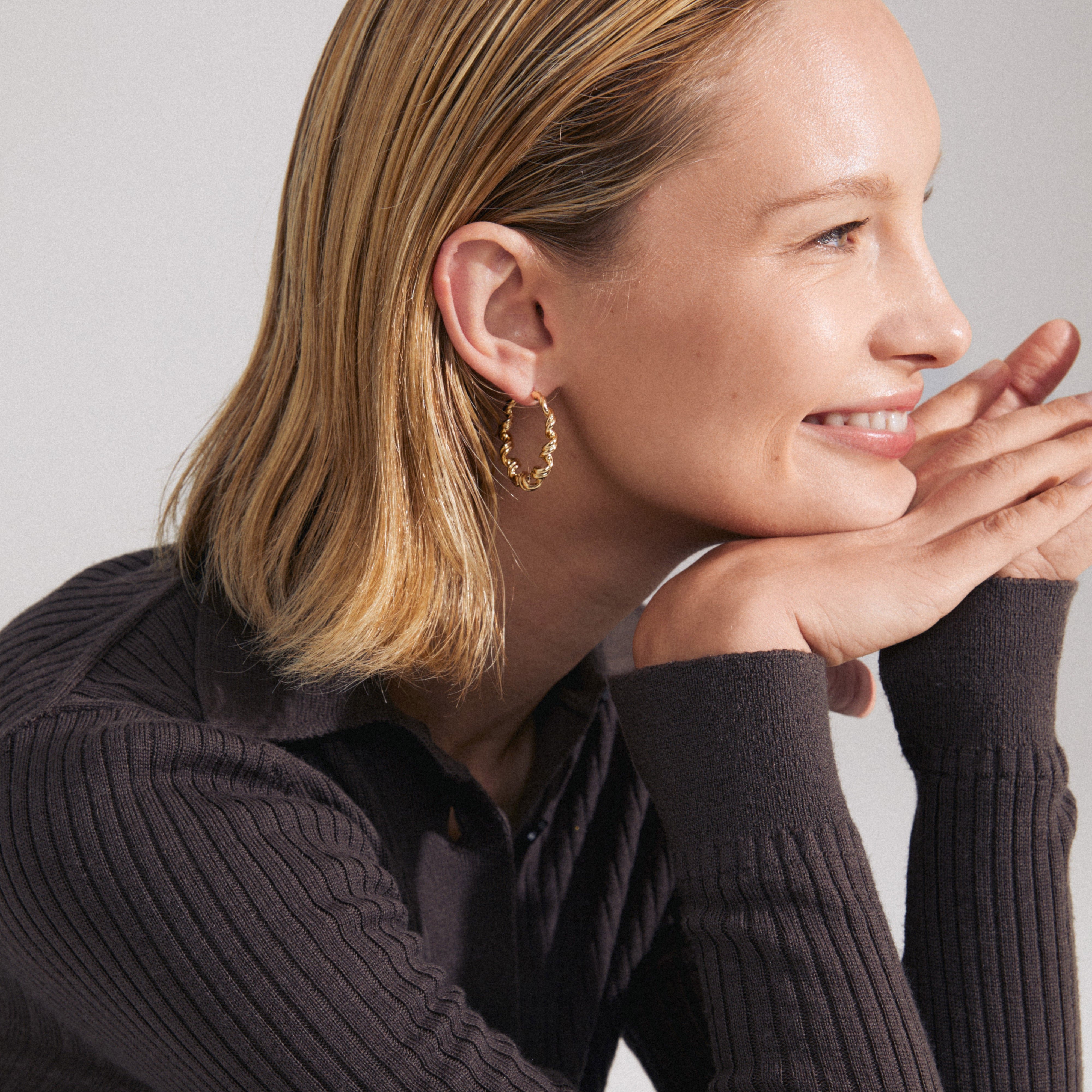 Close-up of a woman's ear wearing gold-plated LARISA hoop earrings with a twisted silhouette from Pilgrim.