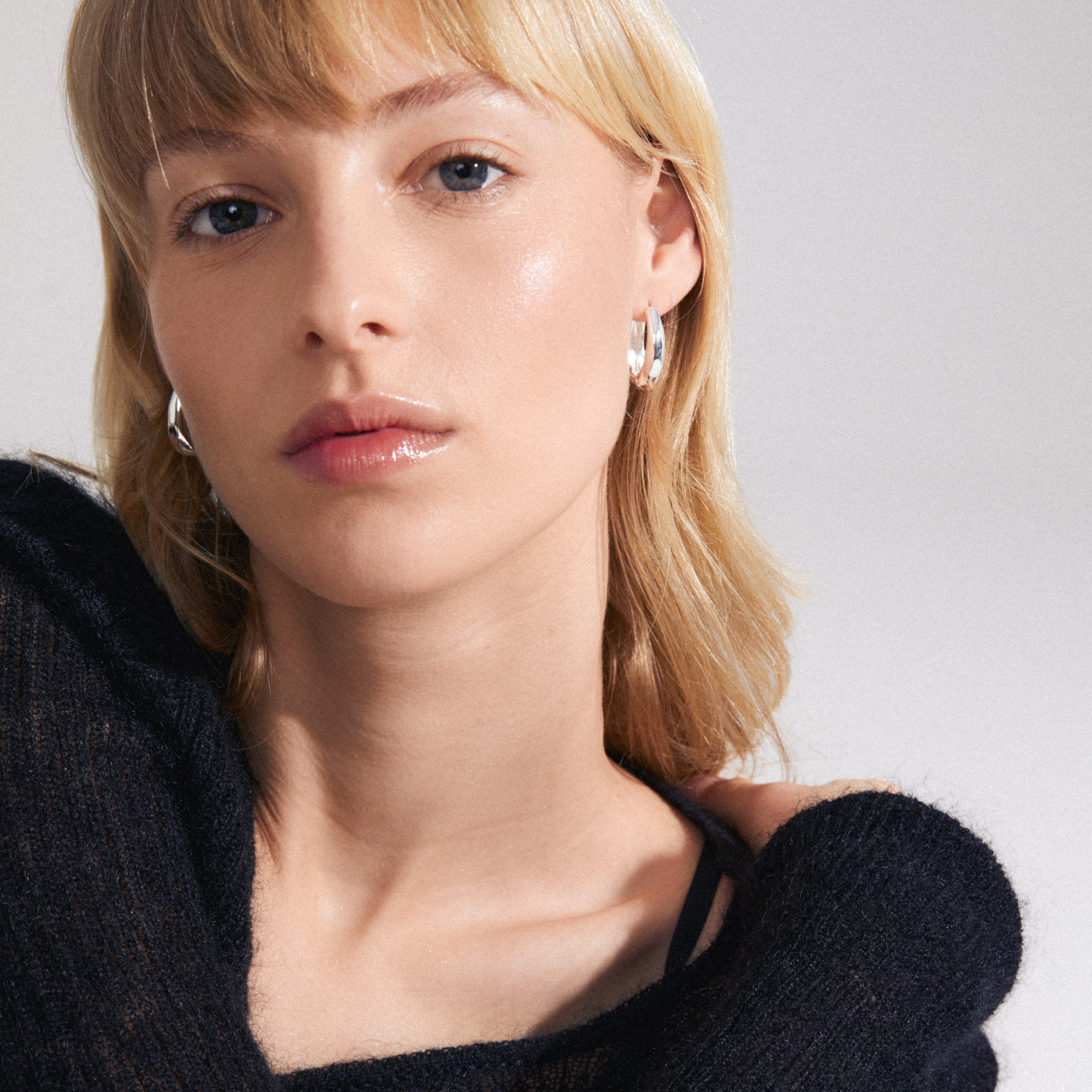 Close-up of a woman wearing ASHER silver-plated earrings, showcasing their chunky, oval design and click clasp.