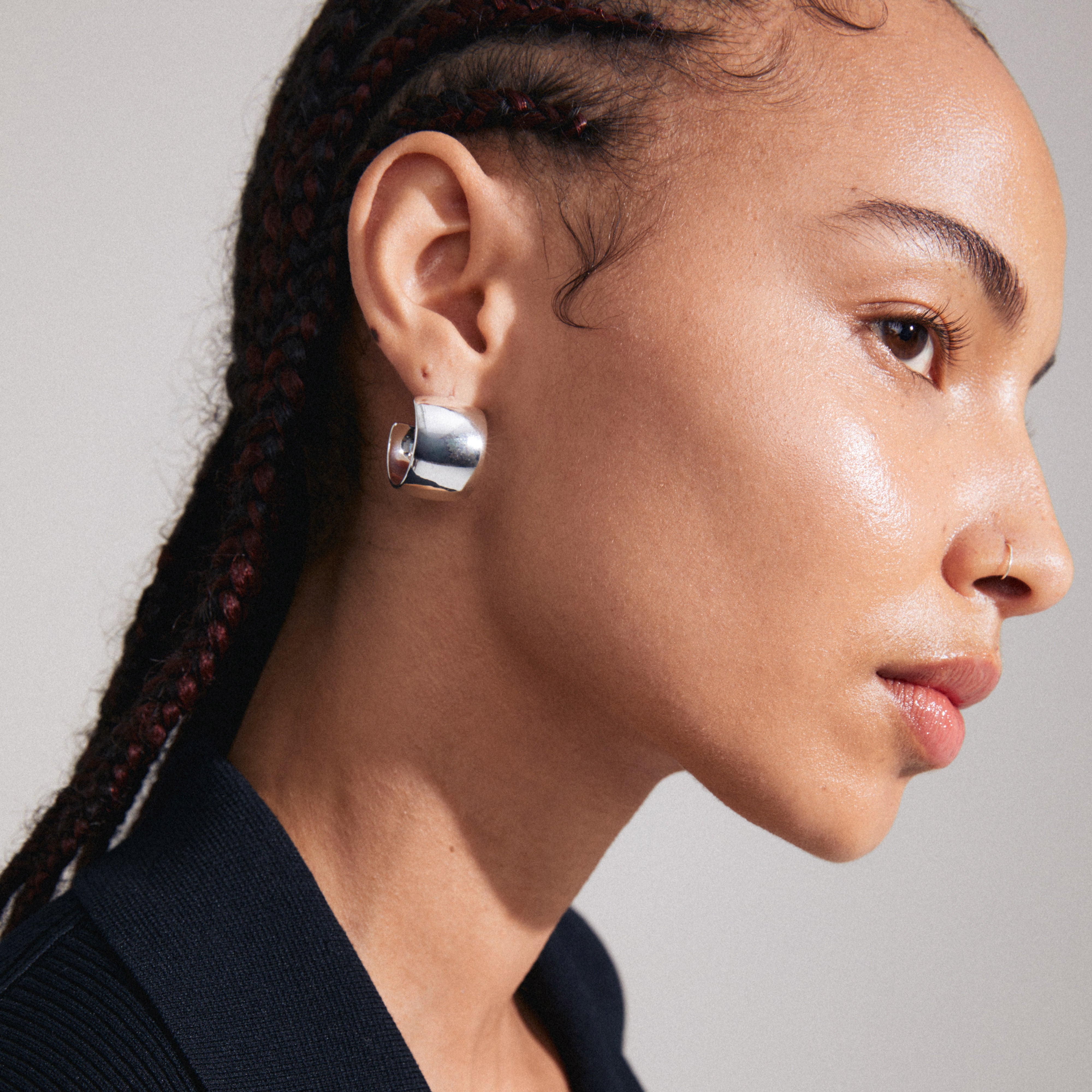 TALULLA earrings silver-plated, ultra-wide hoops on a woman with braided hair, showcasing their glossy shine and trendy, fashion-forward design.