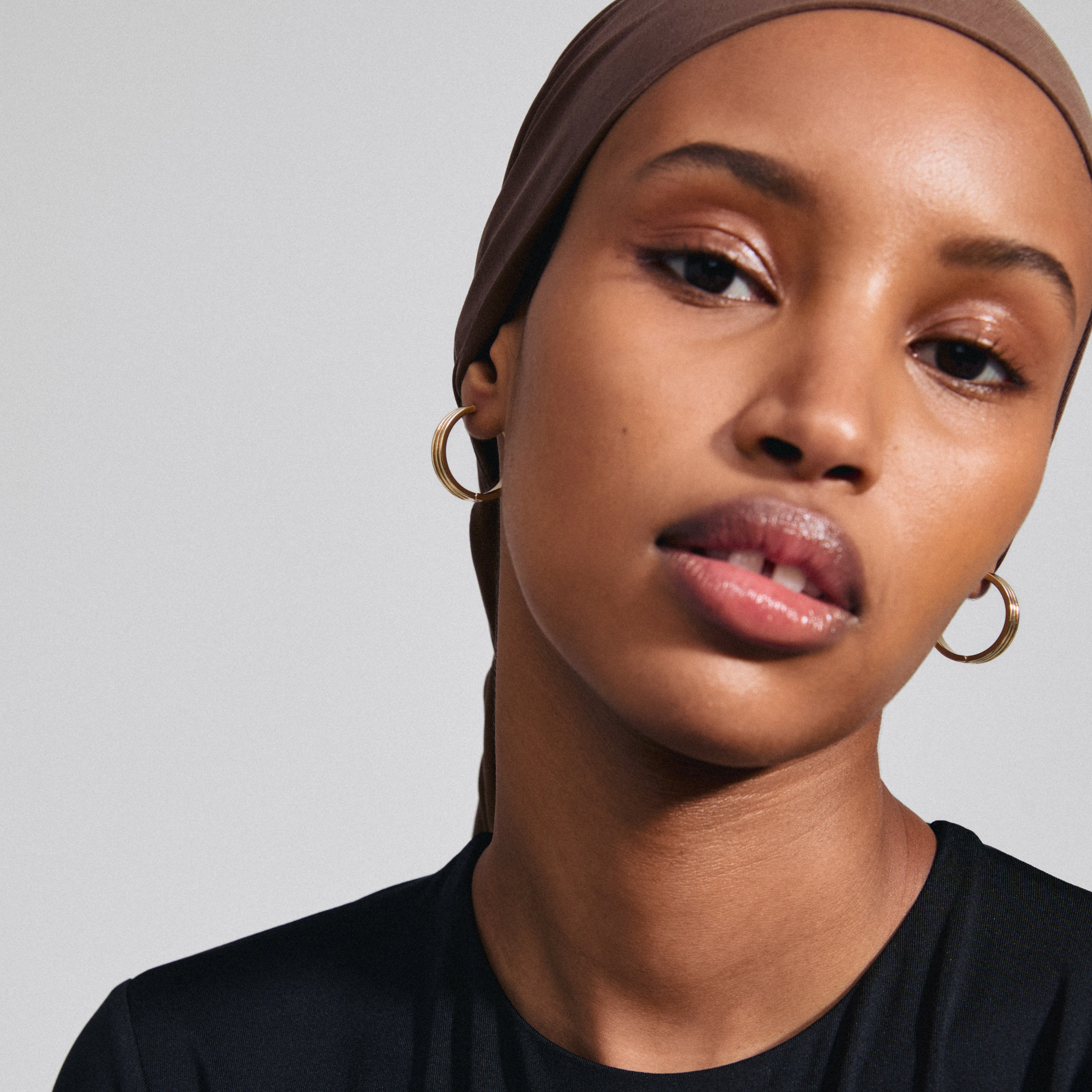 Close-up of a woman wearing BENNETT gold-plated hoop earrings by Pilgrim, showcasing their wide, classic design and easy-to-use click clasp.