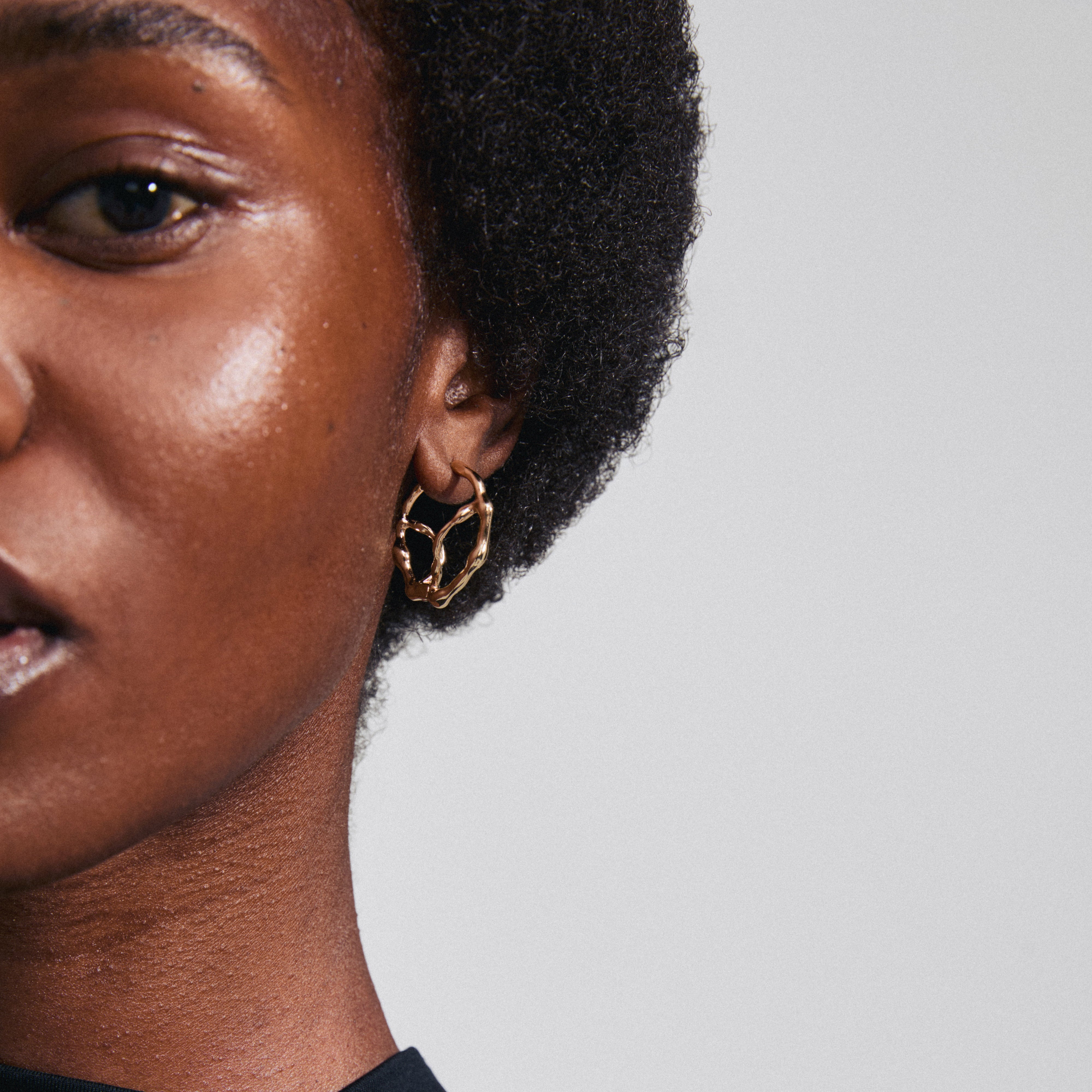 Close-up of a woman's face showcasing Pilgrim's DIDO gold-plated hoop earrings, emphasizing their organic design and modern twist on classic hoops.