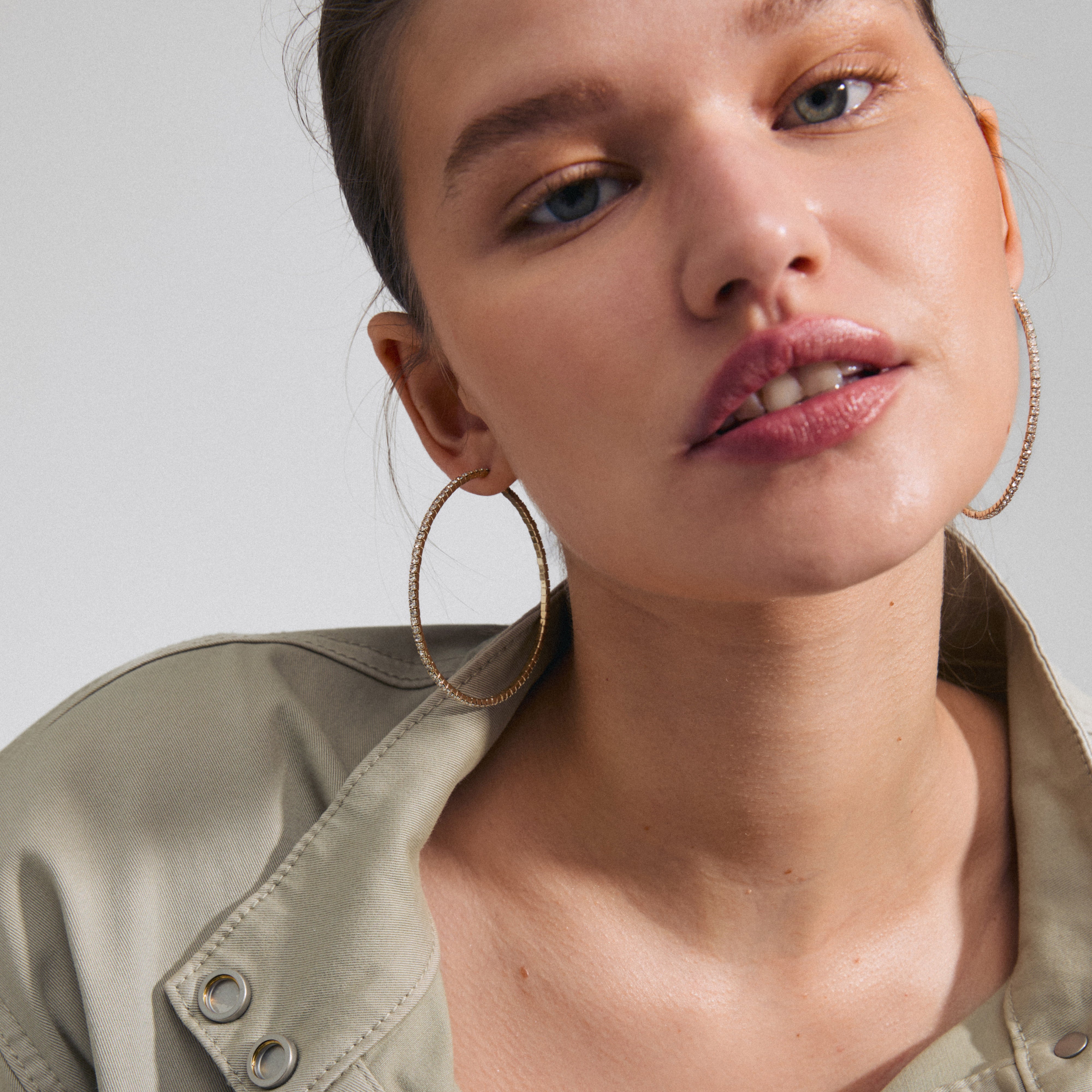 SIDNEY crystal hoop earrings gold-plated by Pilgrim, featuring sparkling Preciosa crystals, worn by a woman with a ponytail, showcasing elegant and trendy fashion.