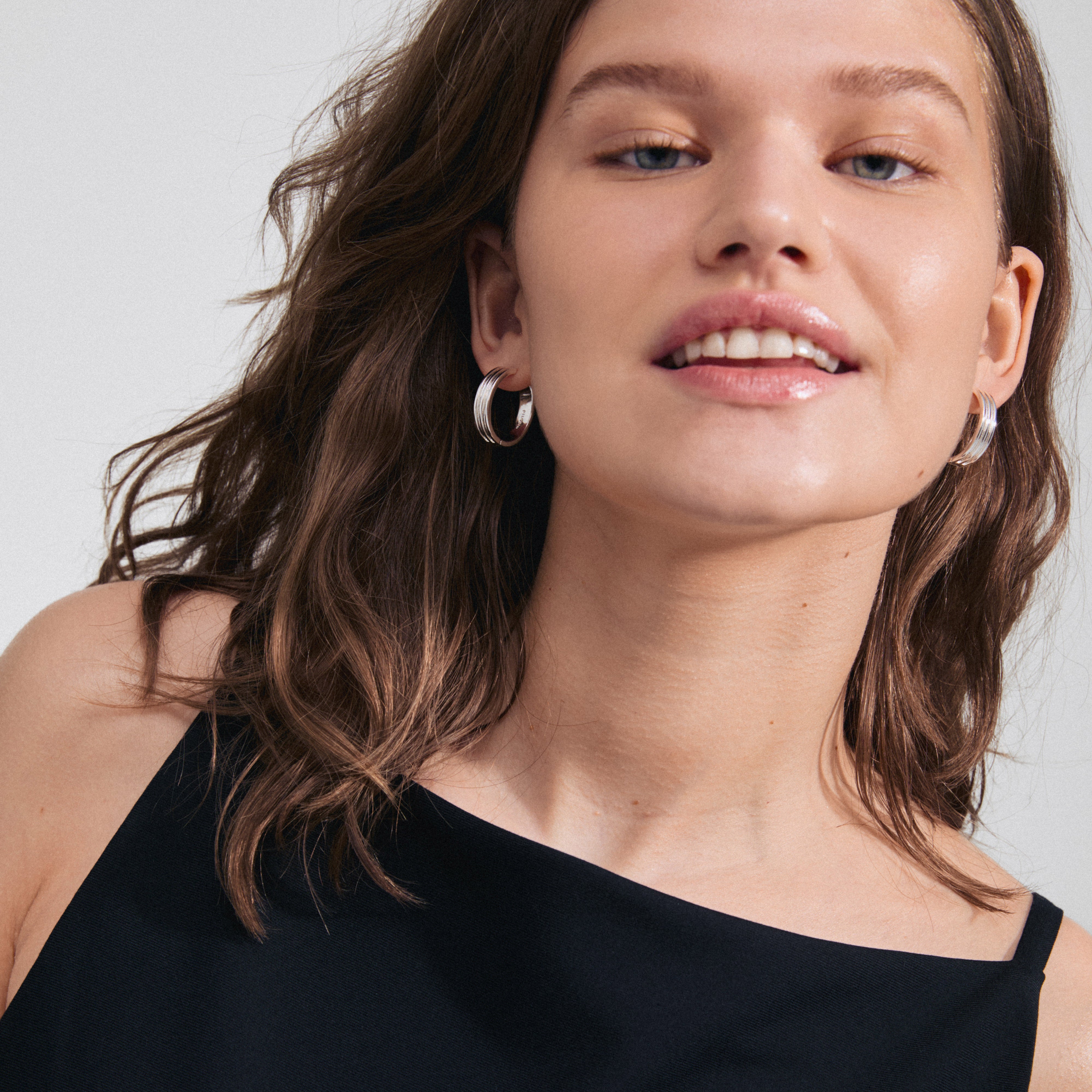 Close-up of a woman wearing BENNETT hoop earrings, silver-plated, showcasing the classic wide design with urban Scandi coolness and easy-to-use click clasp.