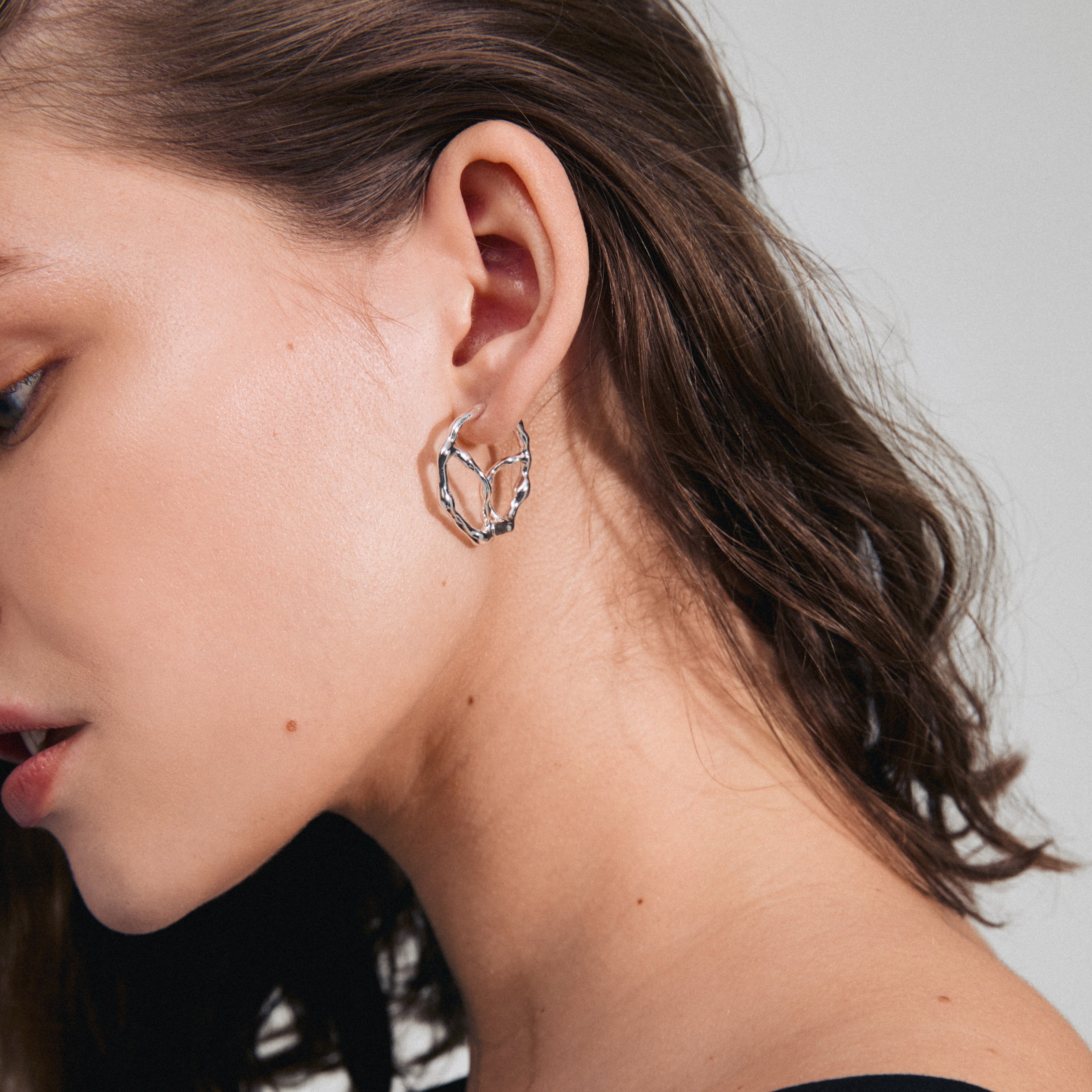 Profile view of a woman wearing DIDO hoop earrings, silver-plated with unique organic detailing, symbolizing modern style and crafted by Pilgrim.