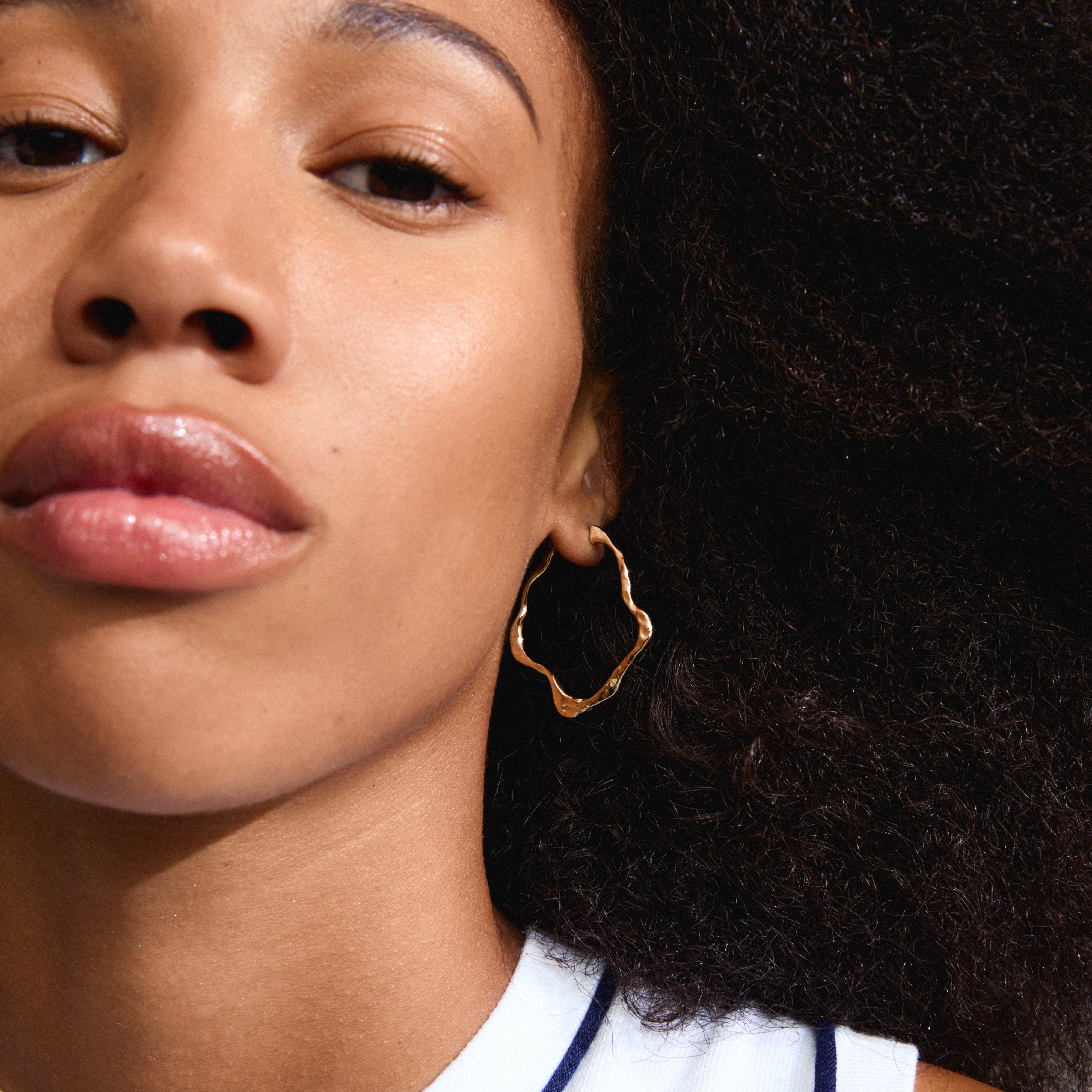Close-up of a woman wearing gold-plated DYLAN earrings, showcasing their unique, organic oval hoop design and glossy finish, part of Pilgrim's IMAGINATION collection.