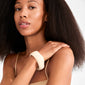 Young woman wearing the AASE maxi bangle beige from Pilgrim, showcasing its chunky, recycled acrylic design on her wrist, embodying a trendy, minimalist Scandi style.