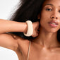 Close-up of a young woman wearing the AASE maxi bangle beige, a chunky off-white recycled acrylic bracelet, showcasing minimalist Scandinavian style and natural beauty.