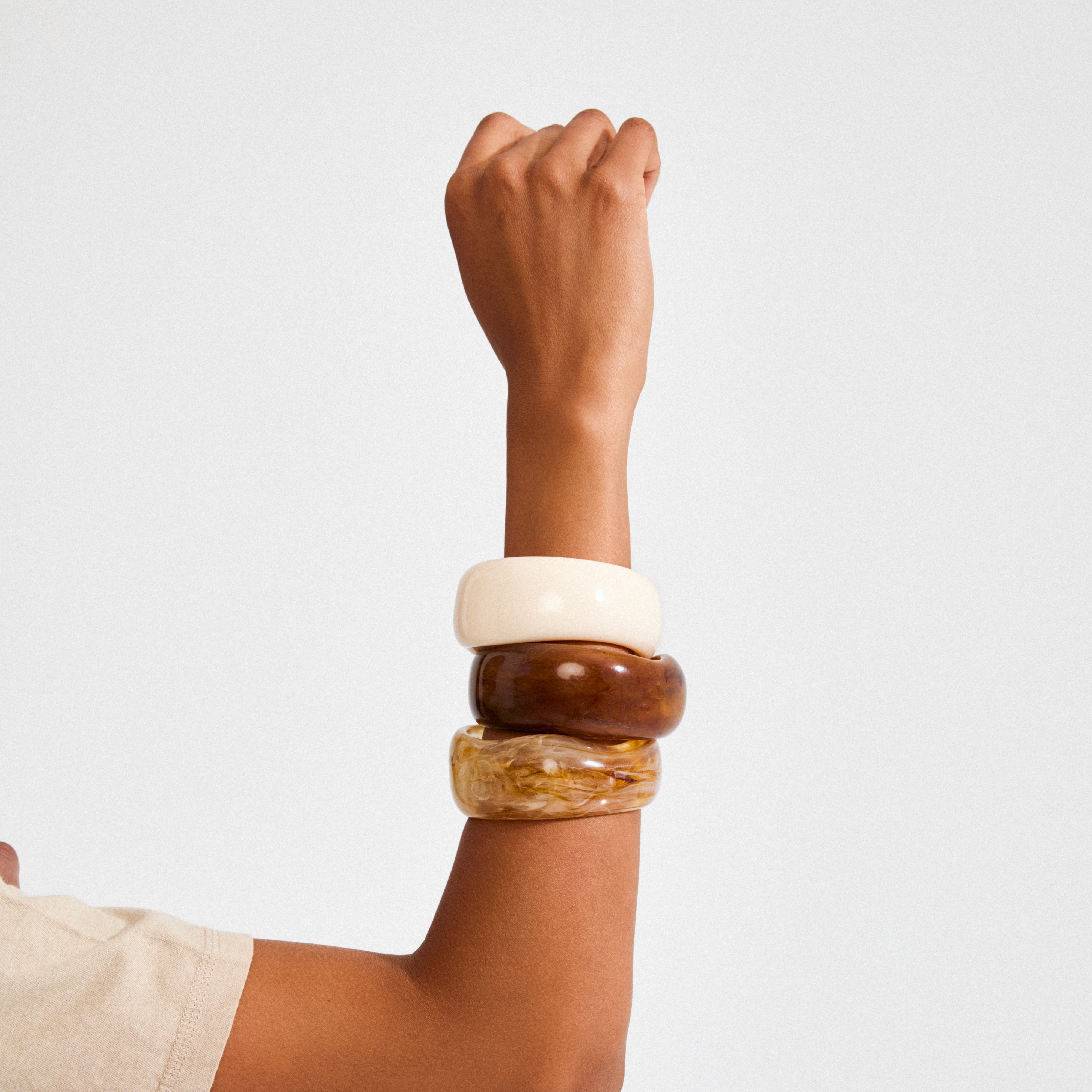 AASE maxi bangle beige: A close-up of a wrist adorned with three chunky bangles, highlighting Pilgrim's recycled ivory bangle for a chic, Scandi-inspired summer look.