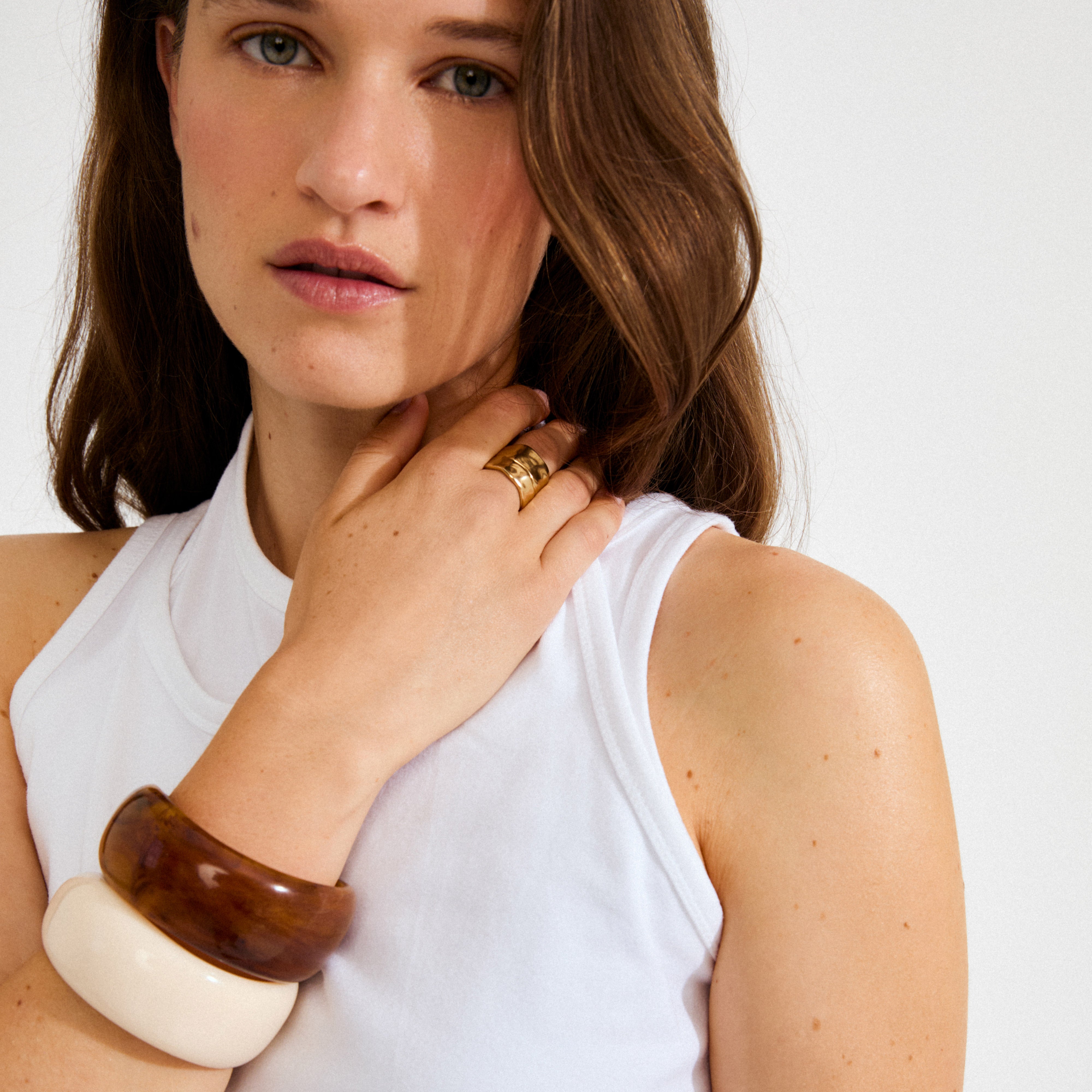 Young woman wearing the AASE maxi bangle beige by Pilgrim, a chunky recycled acrylic bracelet, paired with a tortoiseshell bangle and gold ring.