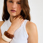 Young woman wearing the AASE maxi bangle beige by Pilgrim, a chunky recycled acrylic bracelet, paired with a tortoiseshell bangle and gold ring.