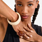 Woman wearing AASE maxi bangle beige, a chunky cream bracelet on her wrist, paired with a large amber-brown ring, showcasing stylish Pilgrim jewelry.