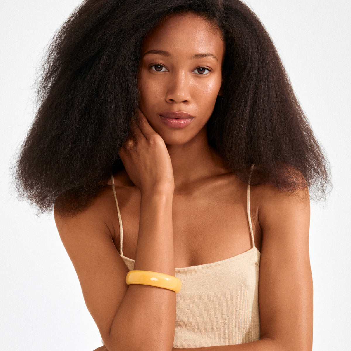 Young woman wearing Pilgrim's AASE bangle in yellow, showcasing its simple Scandi style. Her calm expression and natural hair complement the bracelet's earthy, trendy vibe.