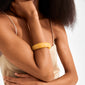 Person wearing a light-beige top with the AASE bangle in warm yellow, showcasing its chunky, smooth design perfect for a trendy, minimalist summer style.