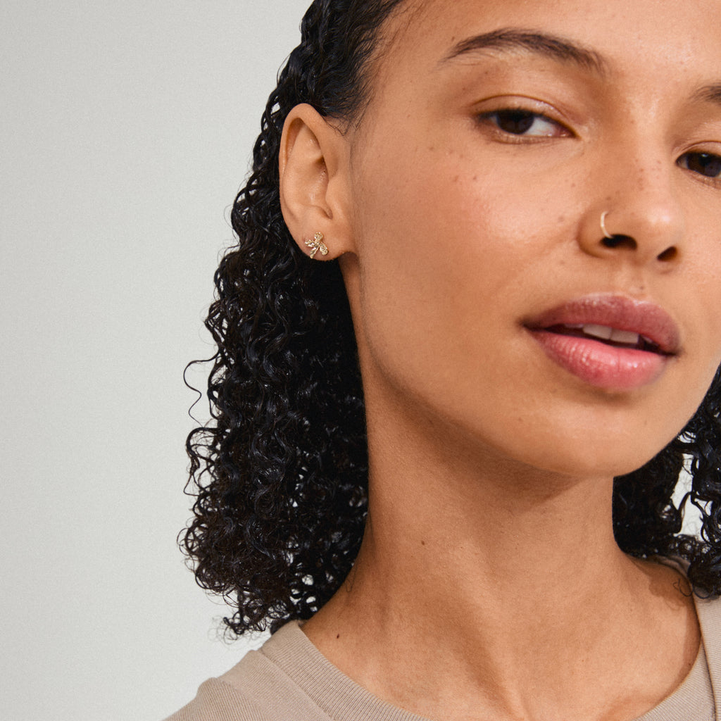 AGLAIA earrings gold-plated on woman with curly hair and nose ring, showcasing delicate flower design inspired by nature, embodying Pilgrim's summer elegance.