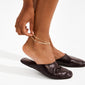 JELONA ankle chain gold-plated with dual Herringbone chains, elegantly layered around the ankle, paired with dark leather slip-on mules, perfect for a chic, summery look.