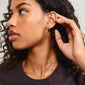 APPOLLONIA earrings gold-plated: A woman with curly hair showcasing the sleek, gold-plated hoops featuring tube-shaped glass beads, perfect for summer style and layering.