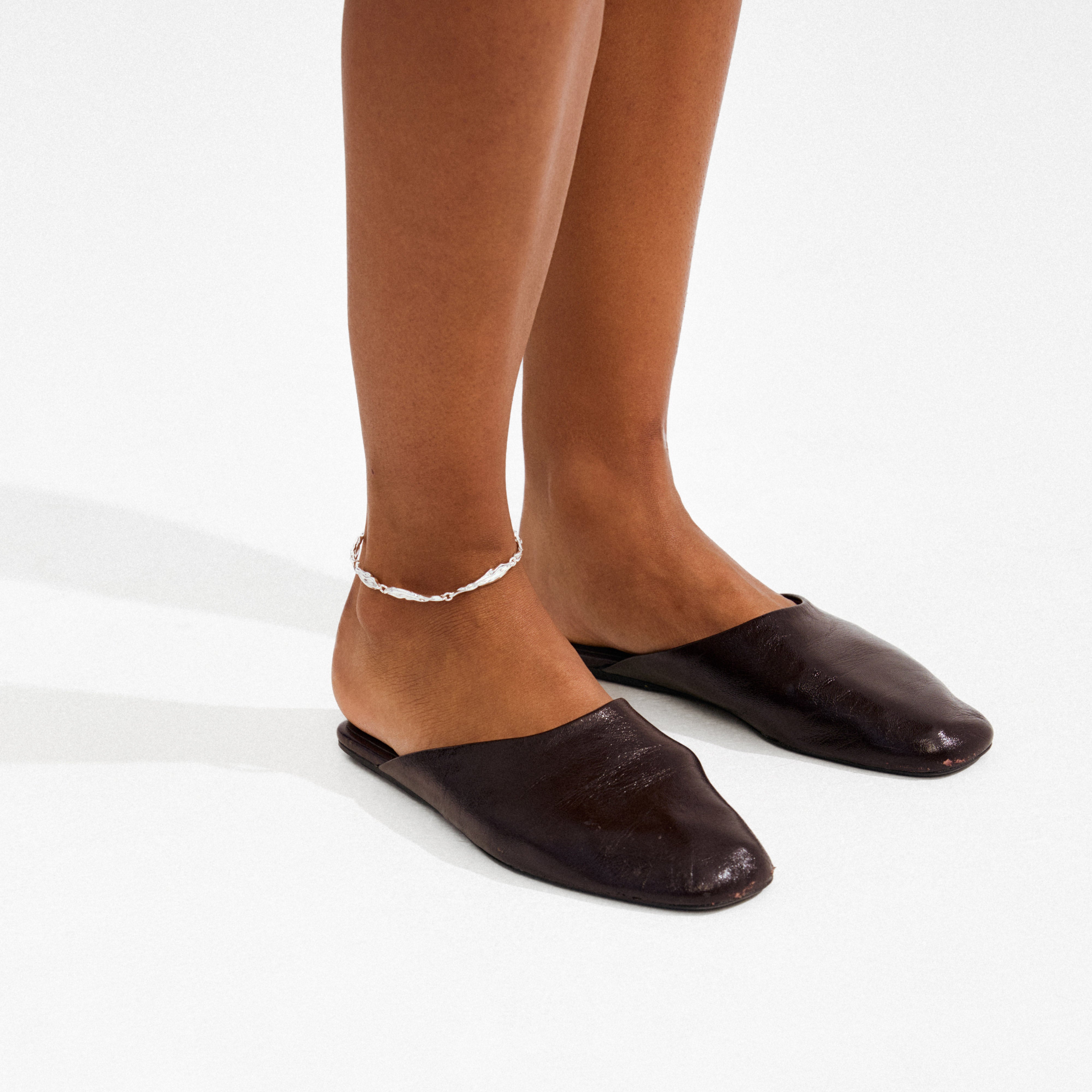 Model wearing brown leather mules and the ARIF silver-plated anklet, featuring elongated organic links, highlighting Pilgrim's trendy, eco-friendly style.