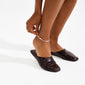 A close-up of a person fastening the silver-plated ARIF anklet from Pilgrim around their ankle, showcasing its organic, nature-inspired design.