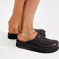 Close-up of someone fastening the JELONA silver-plated anklet with double snake chains around their ankle, paired with a black leather mule in a studio setting.