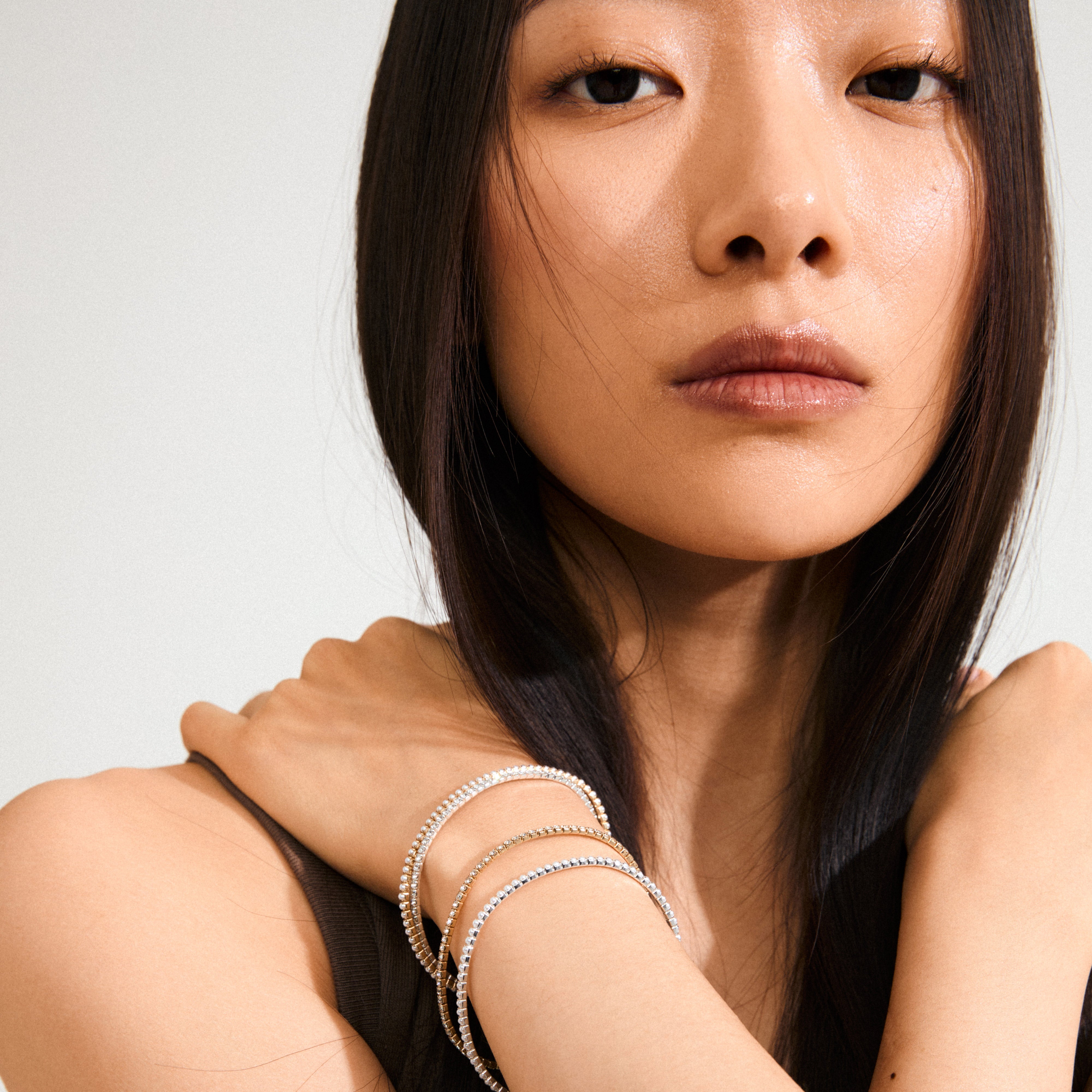 Young woman wearing Pilgrim's ARASH crystal bracelet, gold-plated, stacked with others, showcasing its elegant design and sparkling Preciosa crystals for a chic, minimalist look.
