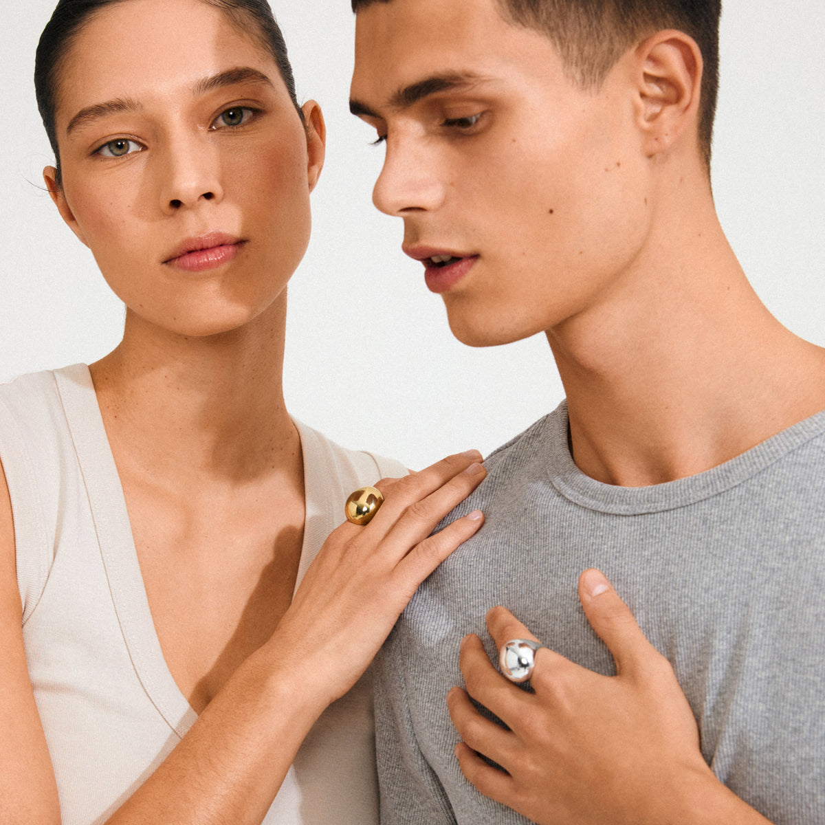 Two young adults wearing minimal attire, highlighting the JAMESON ring. The woman sports a gold-plated, sculptural band ring with a bubble dome design.