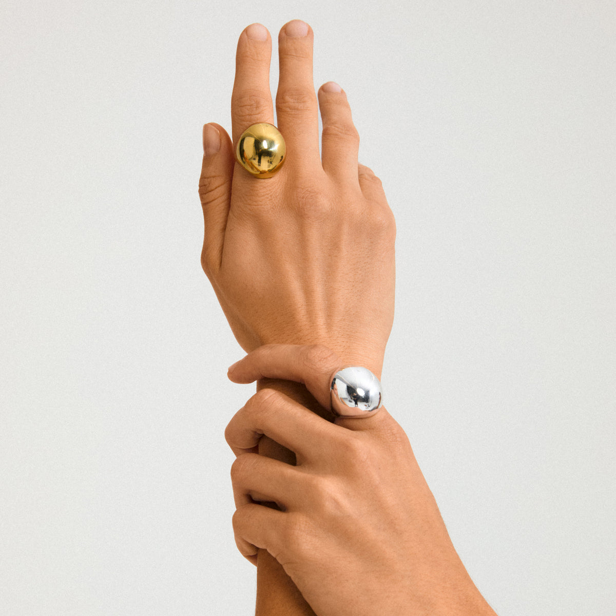 Close-up of two hands wearing Pilgrim's JAMESON ring, featuring a gold-plated, smooth domed design, highlighting its adjustable fit and sustainable, stylish craftsmanship.