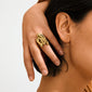 Close-up of a hand displaying the ADRIEL ring, a chunky, gold-plated piece with a fluid, sculptural design, resting gracefully on the middle finger.