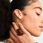 Close-up of a hand wearing the LIAN ring gold-plated/brown, showcasing its chunky, organic design against a dewy, highlighted neck and textured hair.