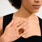Woman wearing the LIAN ring: a gold-plated, amber-colored, sculptural statement piece on her middle finger, showcasing its bold, organic design.