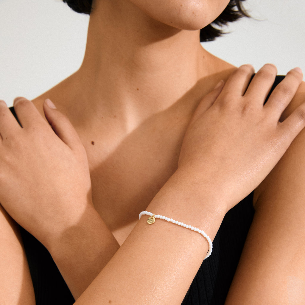 Woman showcasing the INDIE bracelet with white faceted glass beads and gold-plated details, highlighting its elegance and versatility for stacking.