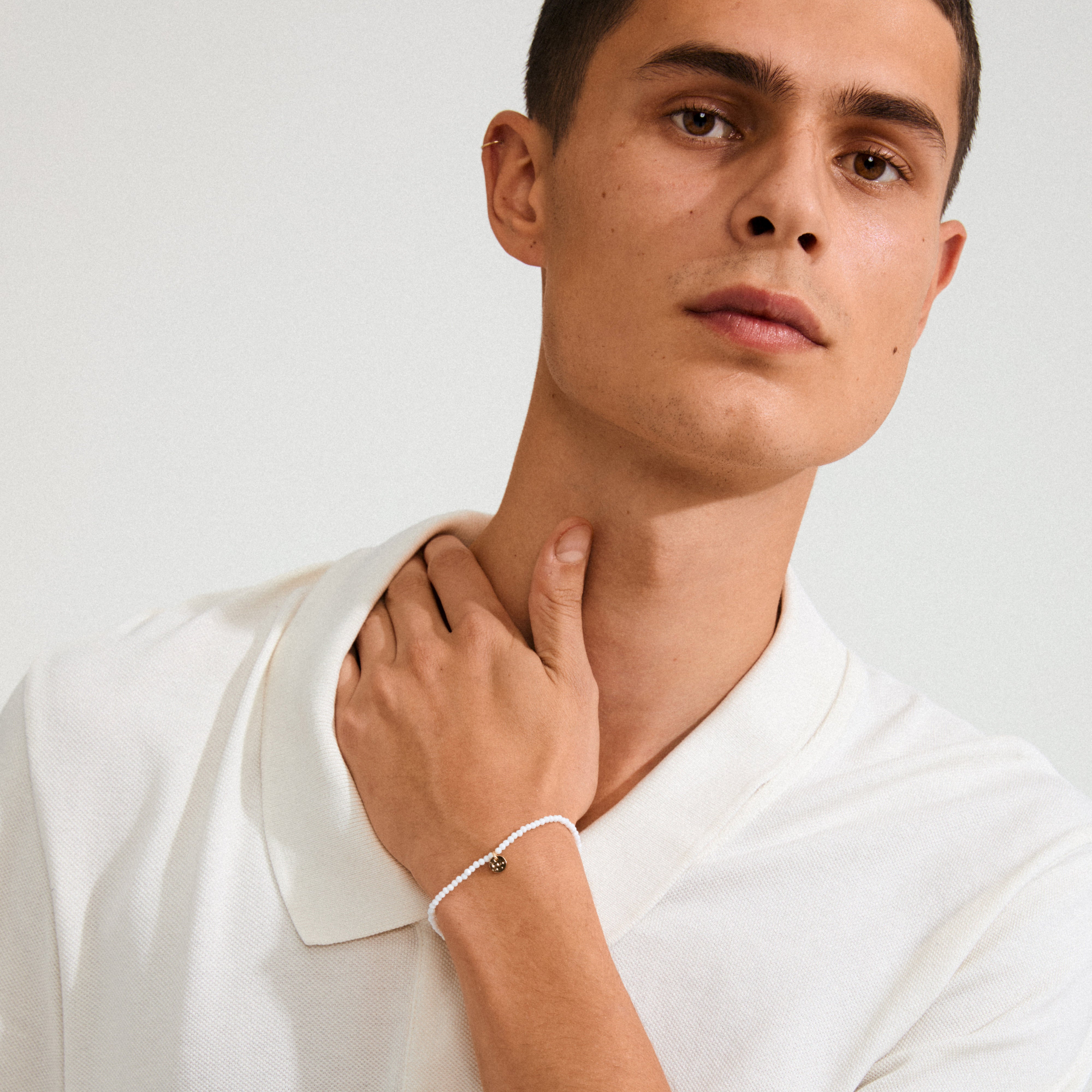 Man wearing the INDIE bracelet, featuring white faceted glass beads and a gold-plated logo, highlighting its stylish design and perfect fit on the wrist.
