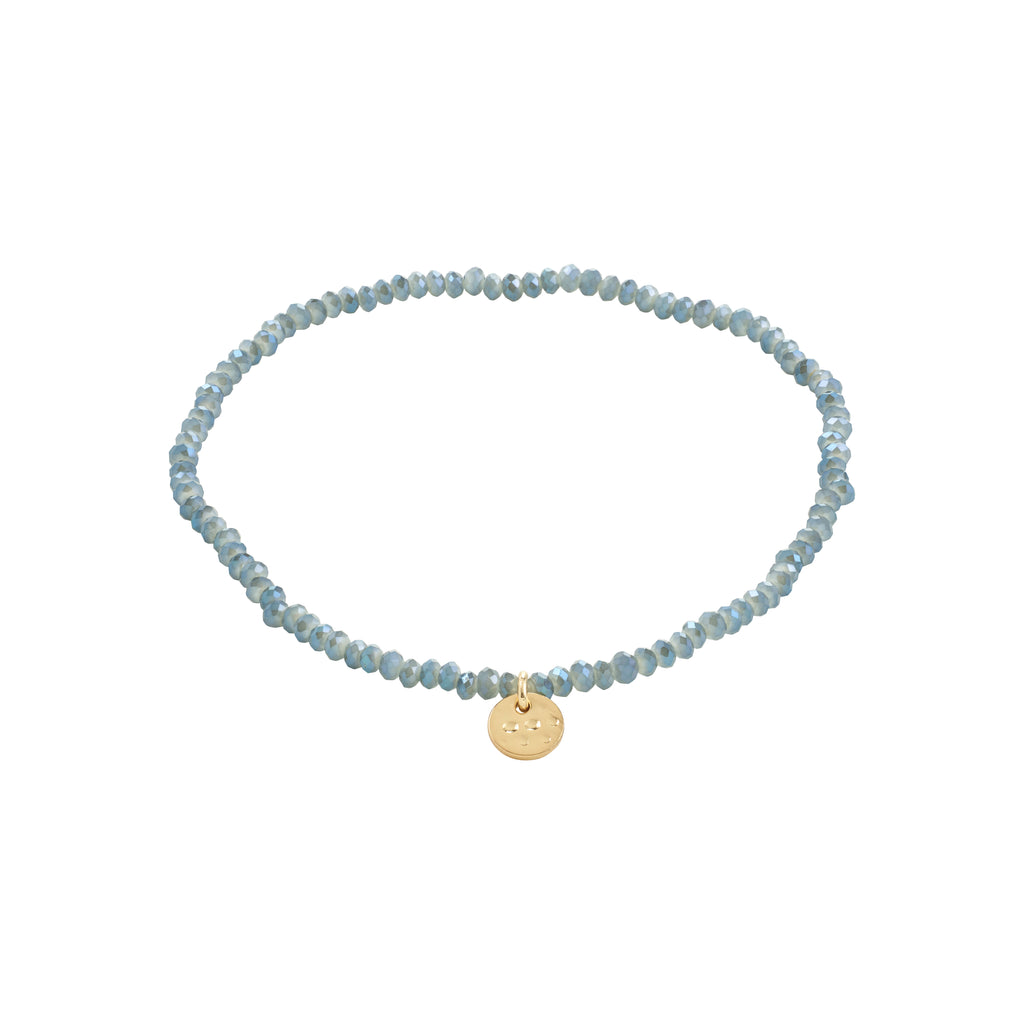 INDIE bracelet dusty blue: A blue beaded bracelet with a gold-plated disc, featuring faceted glass beads on elastic for versatile, stylish wear.