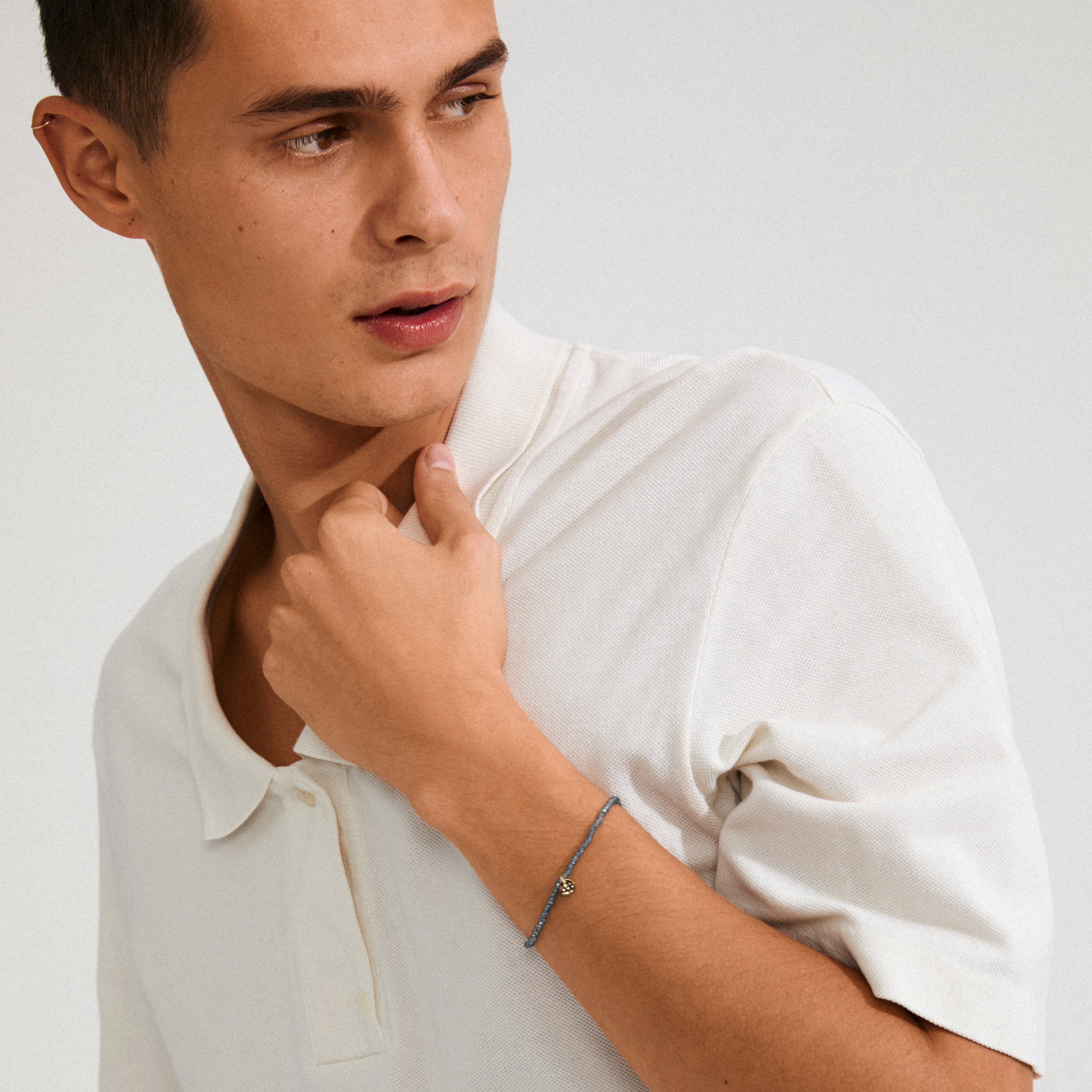 Close-up of a man wearing the INDIE bracelet in dusty blue with gold-plated accents, highlighting its faceted glass beads and Pilgrim logo.