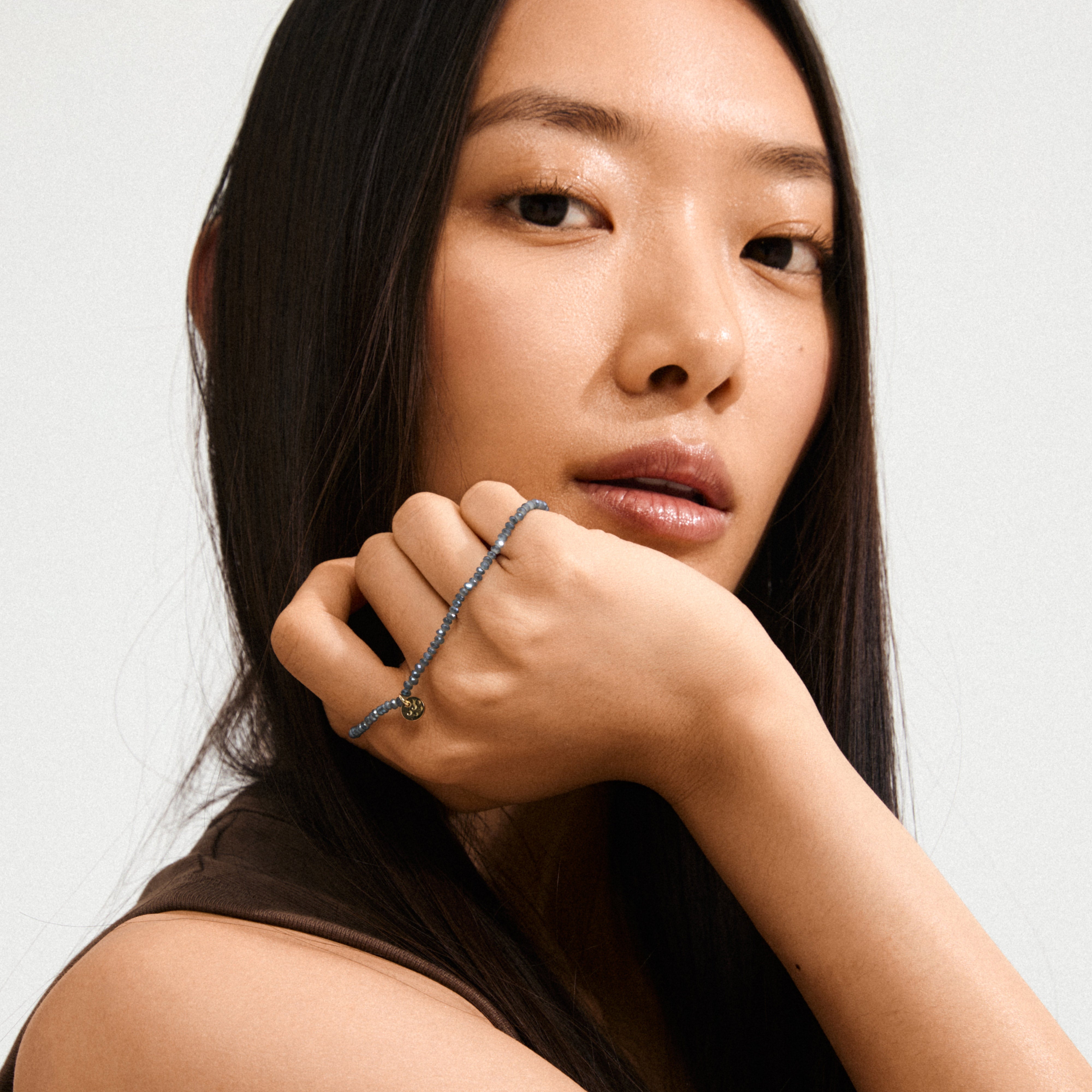 Woman wearing the INDIE bracelet, featuring dusky blue faceted glass beads and a gold-plated logo, highlighting its elegant design on her wrist.