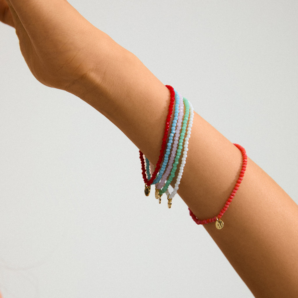 Person's forearm wearing Pilgrim's INDIE bracelet in mint green, featuring faceted glass beads and a gold-plated charm, perfect for stacking.