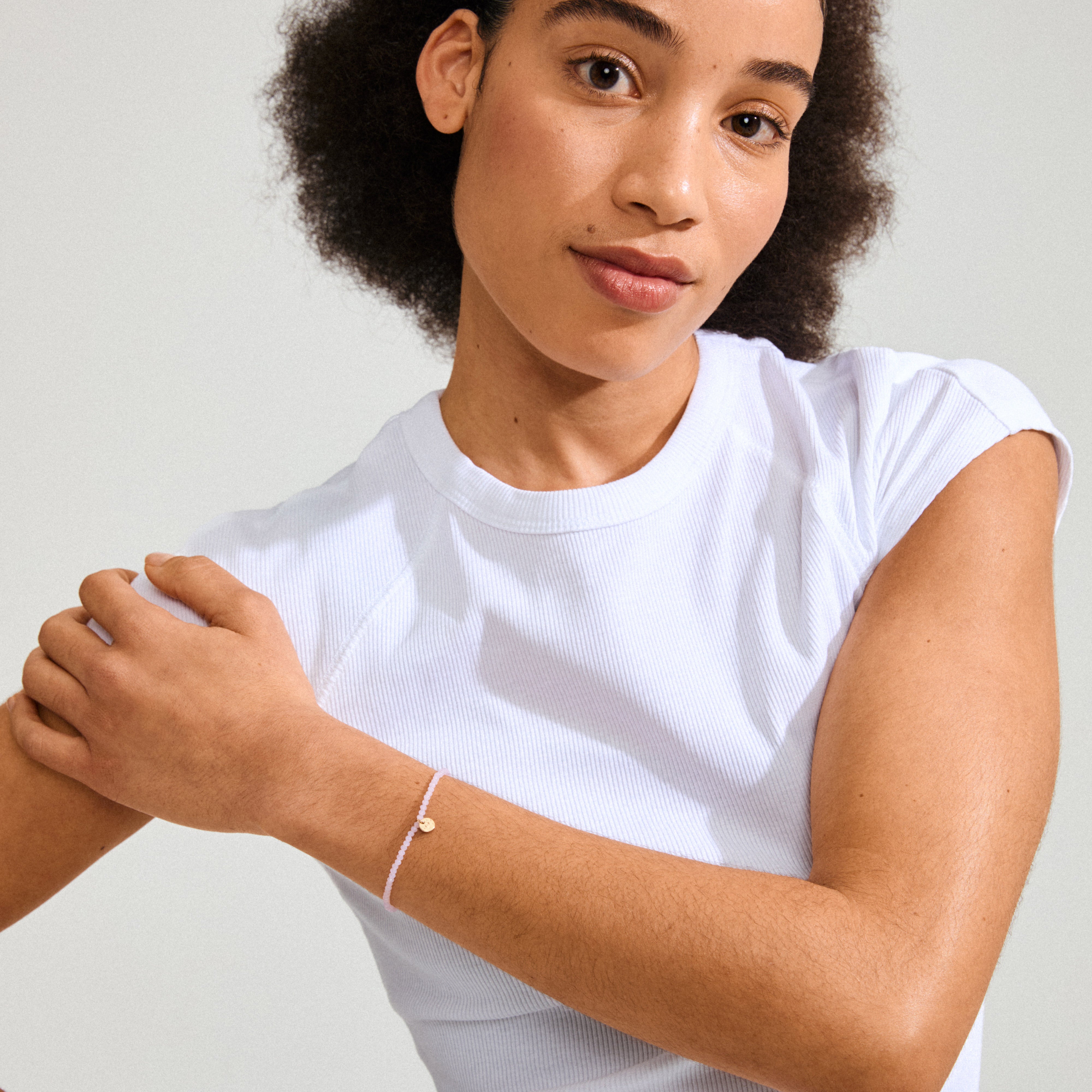 Woman wearing a white shirt showcases the INDIE bracelet, featuring rose faceted glass beads and a gold-plated Pilgrim logo, highlighting its elegant design.