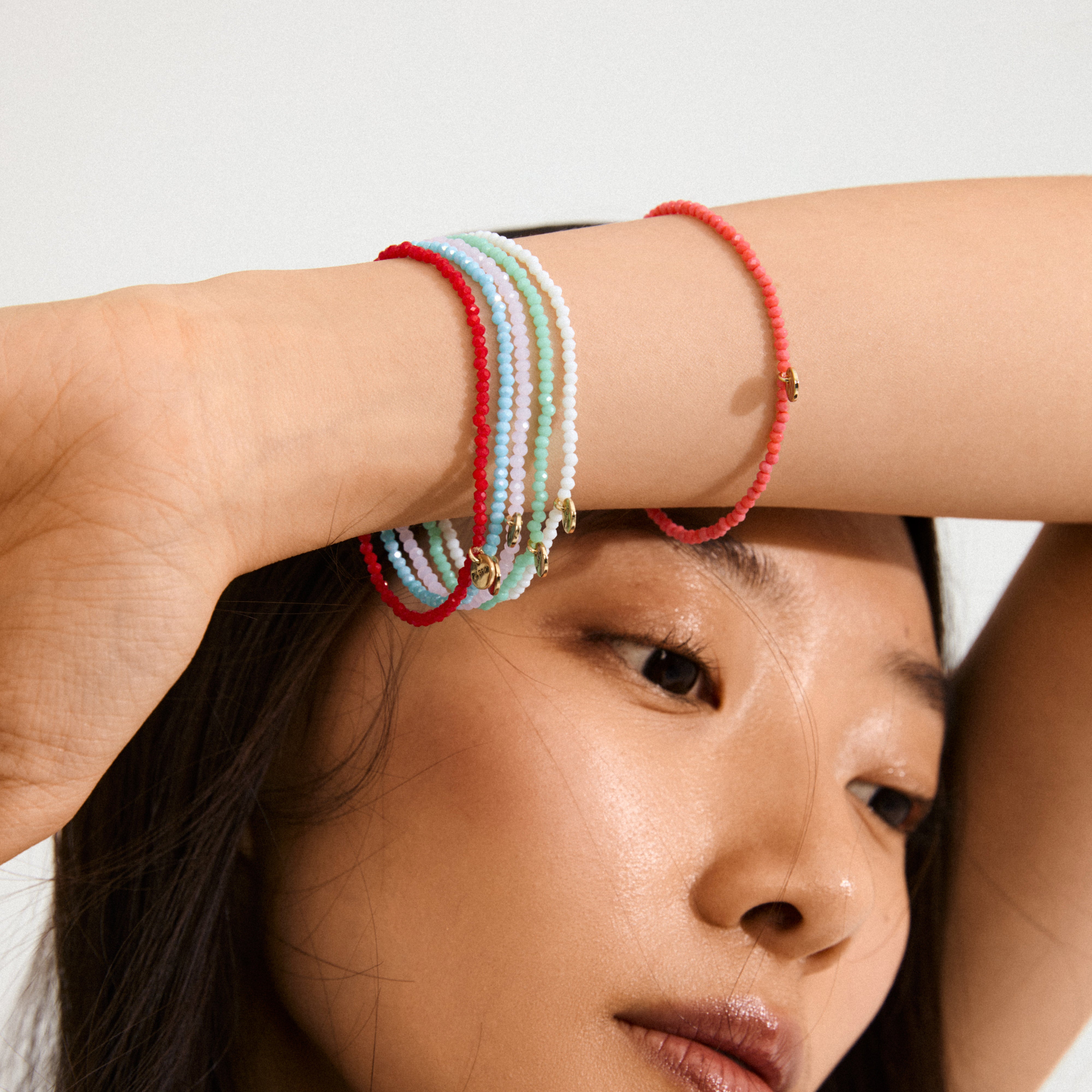 Woman wearing INDIE bracelet with rose faceted glass beads and gold-plated charms, showcasing its elegance and versatility, perfect for stacking and personal style.