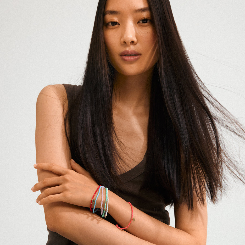 Young person wearing the INDIE bracelet with rose faceted glass beads and gold-plated logo, showcasing layered, stylish bracelets on one wrist against a plain background.
