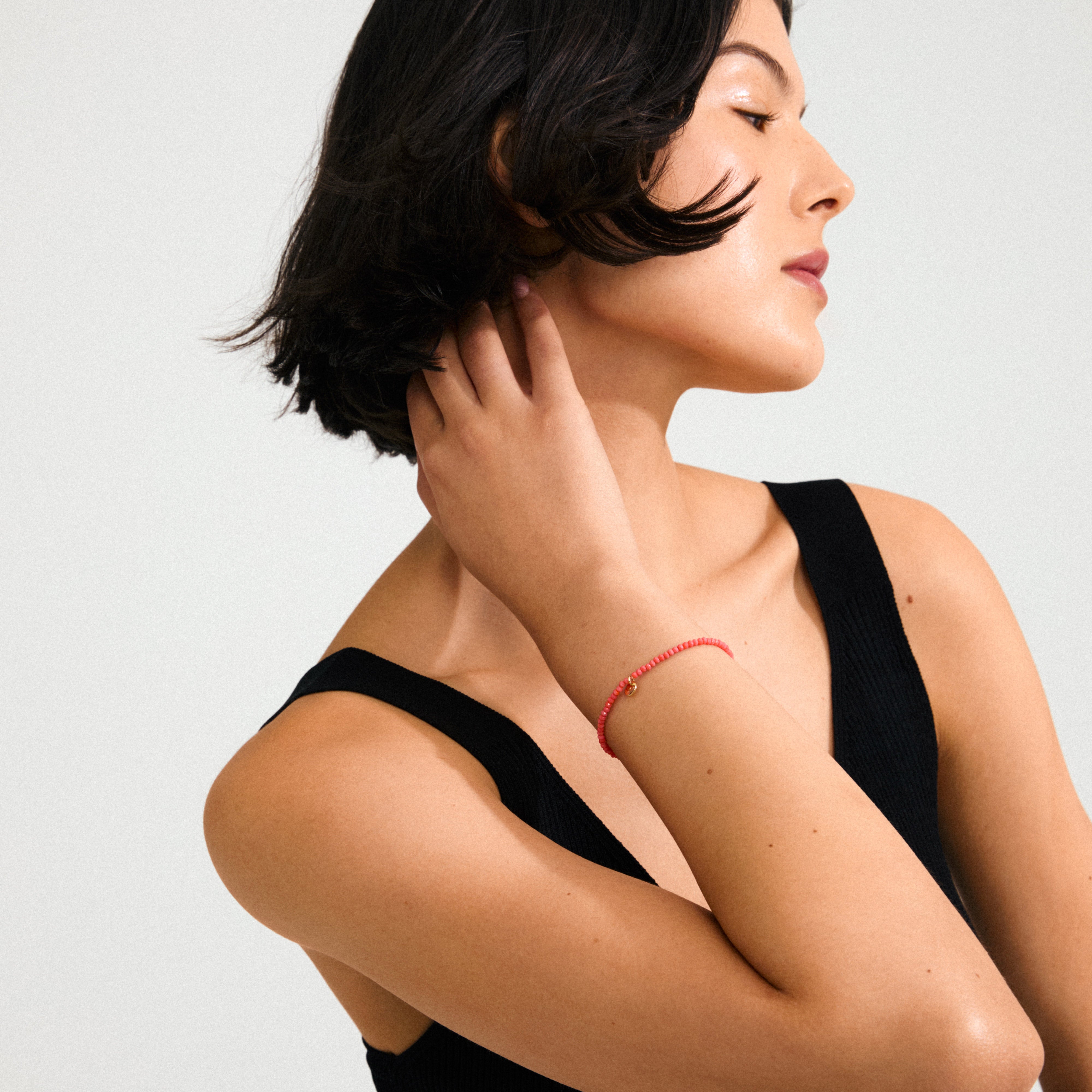 Close-up of the INDIE bracelet with peach-hued faceted glass beads and gold-plated logo, worn on a woman's wrist, showcasing its elegant design.