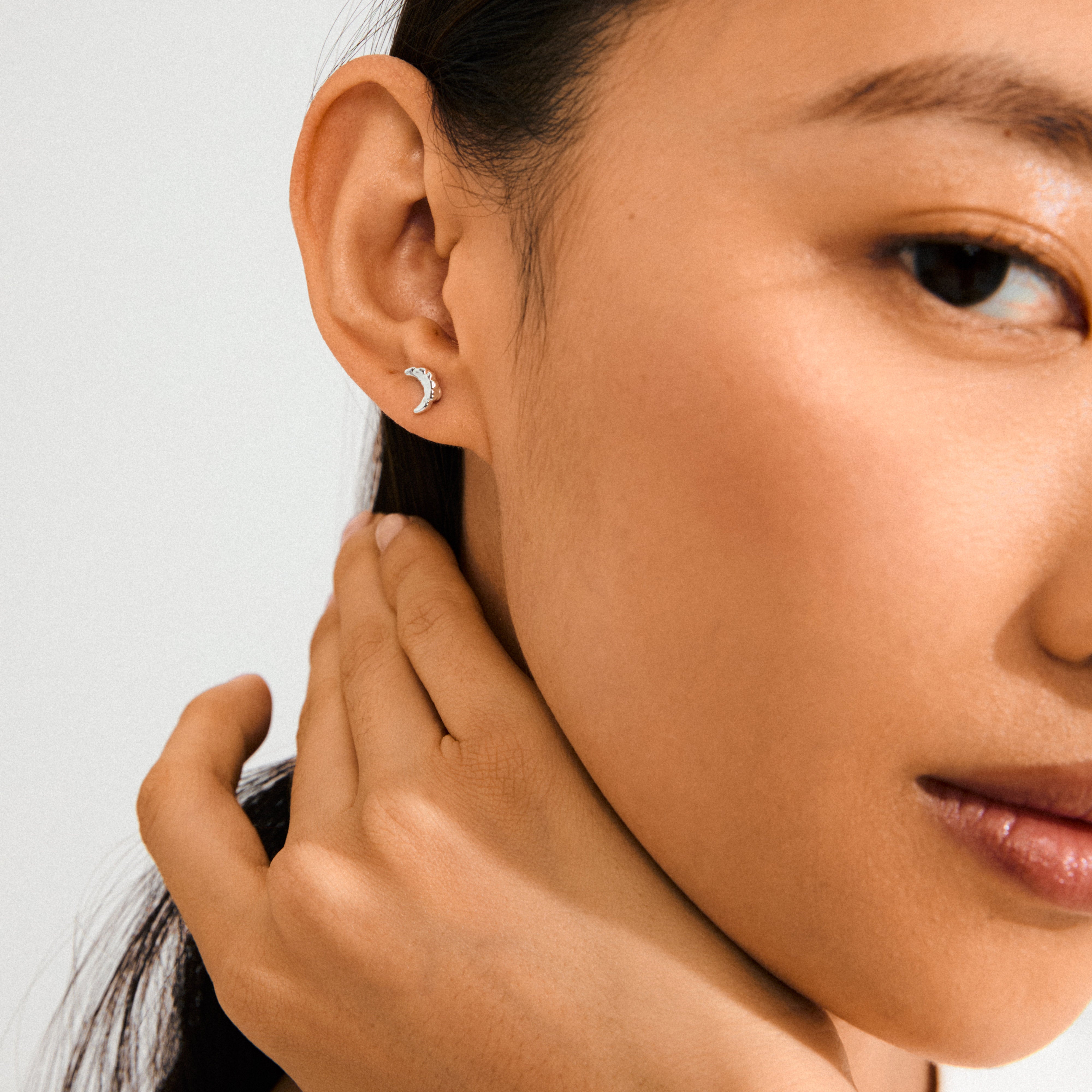 Close-up of a woman's face wearing silver-plated crescent moon earrings, highlighting the whimsical and minimalist design by Pilgrim.