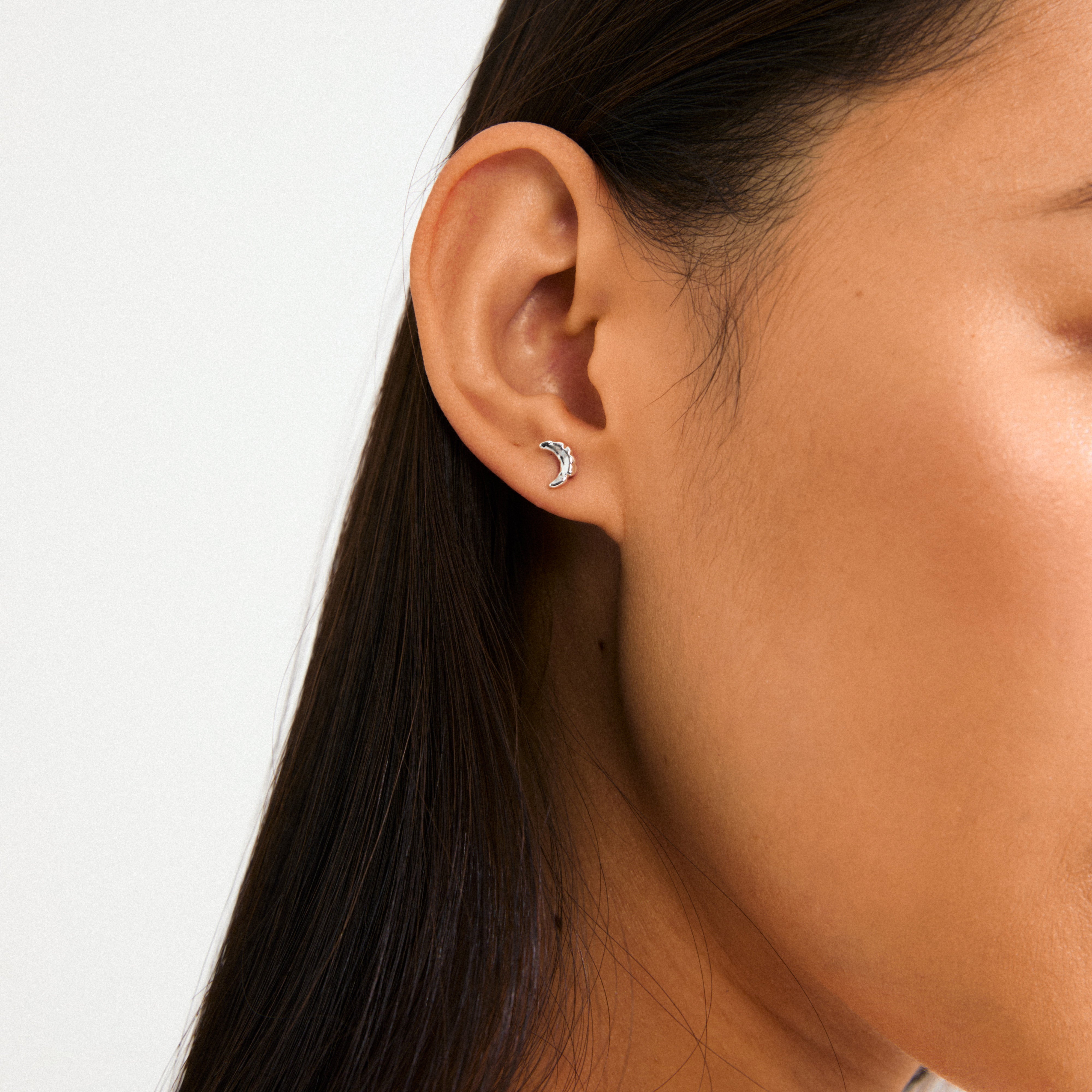 Silver-plated crescent moon stud earrings adorn a woman's ear, showcasing Pilgrim's blend of trendy and timeless design, perfect for casual or evening wear.