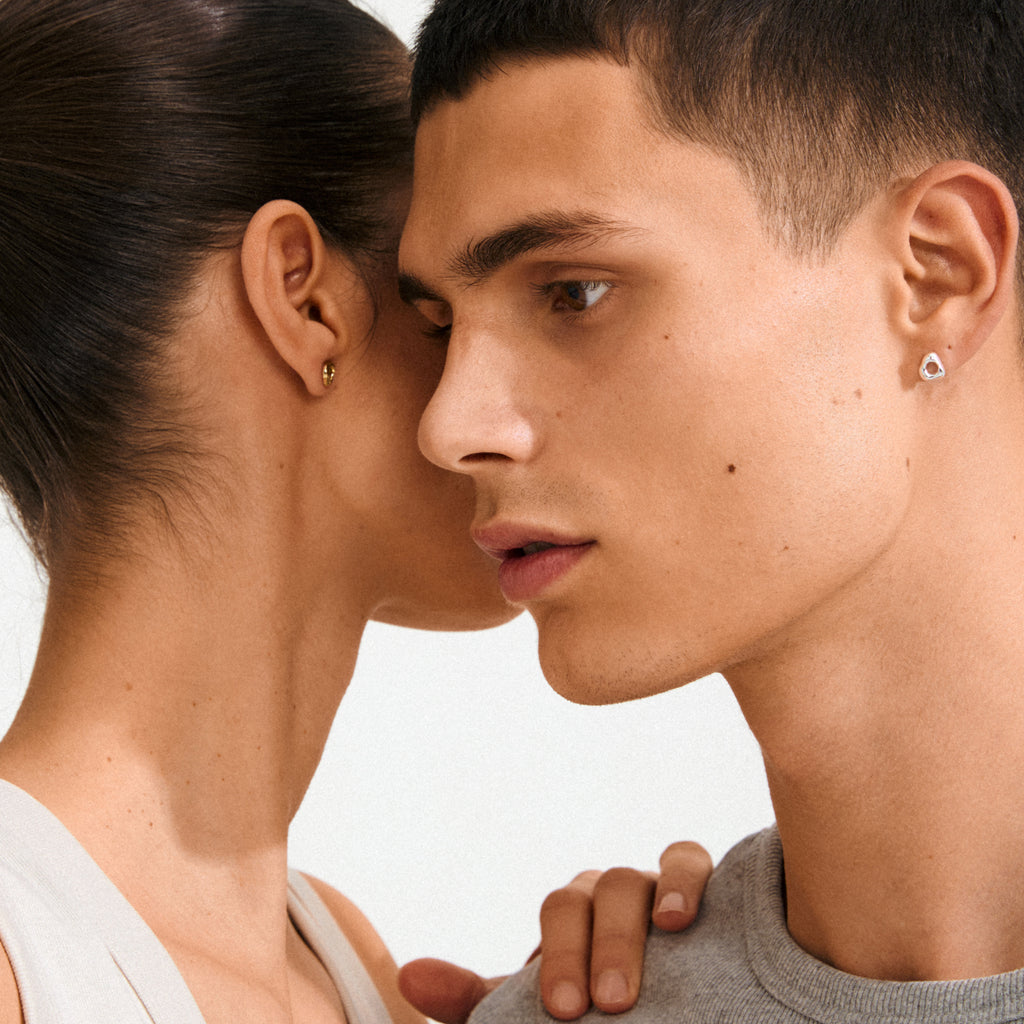 Close-up of a couple, focusing on the man’s profile wearing FREE earrings silver-plated, a small, shiny stud with an organic shape, embodying Pilgrim's elegant style.