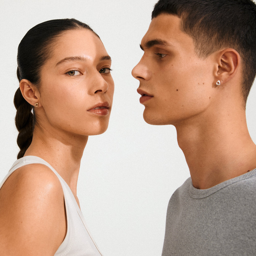 Two young adults display FREE earrings silver-plated by Pilgrim, showcasing small, silver-plated stud earrings with an organic, raw design and central hole.