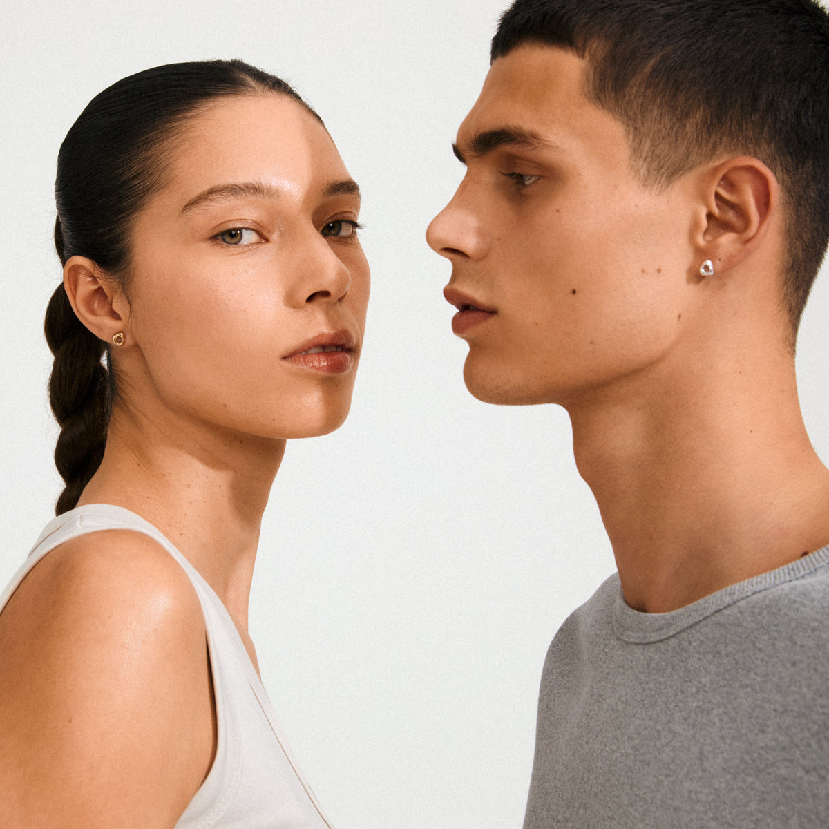 Two young adults display FREE earrings silver-plated by Pilgrim, showcasing small, silver-plated stud earrings with an organic, raw design and central hole.