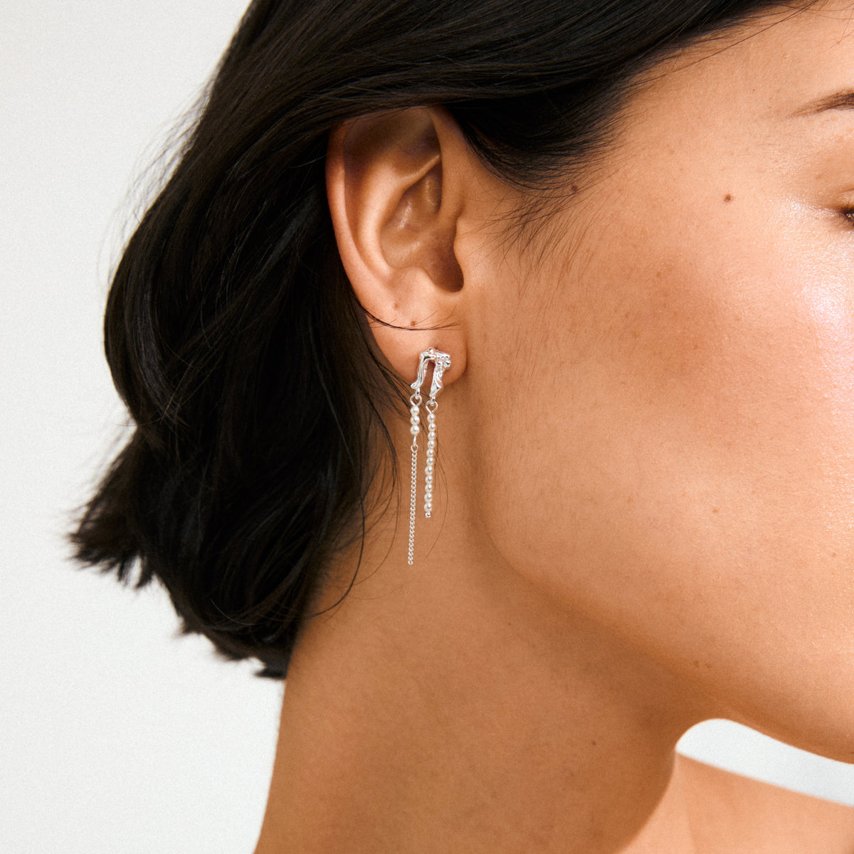 Close-up of ear wearing VINCENT earrings silver-plated from Pilgrim, featuring a knotted cluster and three delicate chains with bead accents, exuding fairytale elegance.