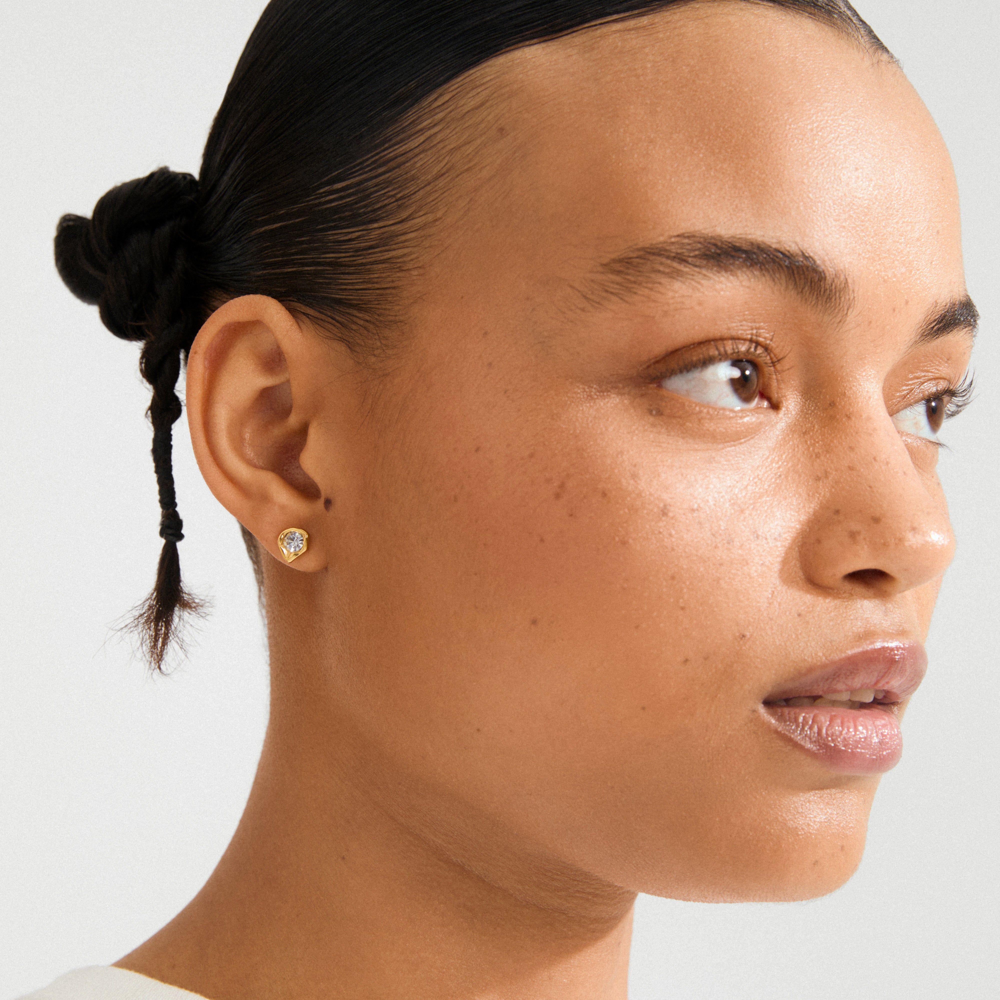 Close-up of a person wearing the KOTA gold-plated earrings by Pilgrim, featuring a wavy setting and sparkling Preciosa crystal in a sleek, stylish design.