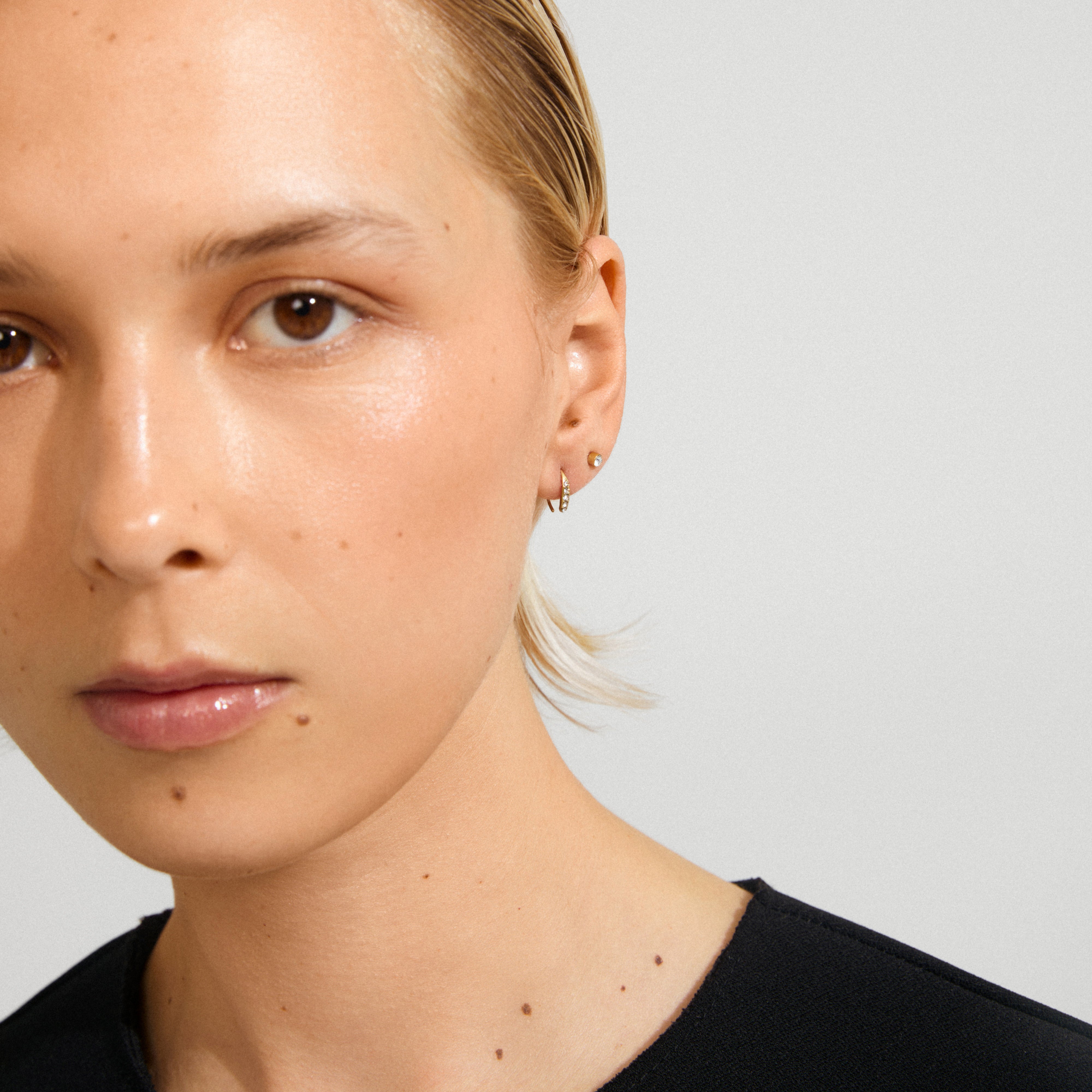 GIONNI earrings 2-in-1 set, gold-plated, featuring a stud with Preciosa crystals and a thin hoop, worn on a person with slicked-back hair.