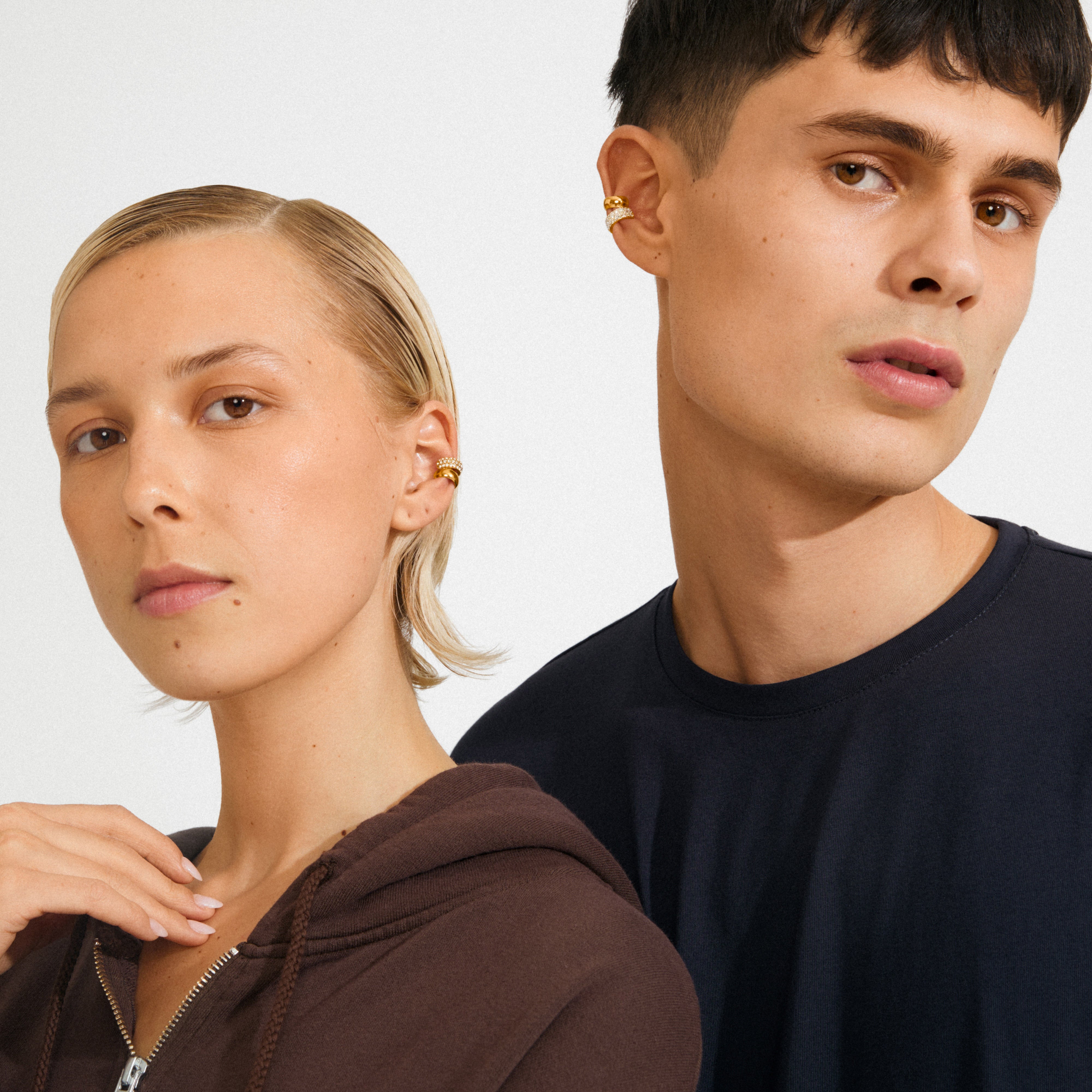 Two models showcase HUDSYN ear cuffs, a gold-plated 2-in-1 set, embodying an edgy, chic style. The man and woman each wear matching ear cuffs.