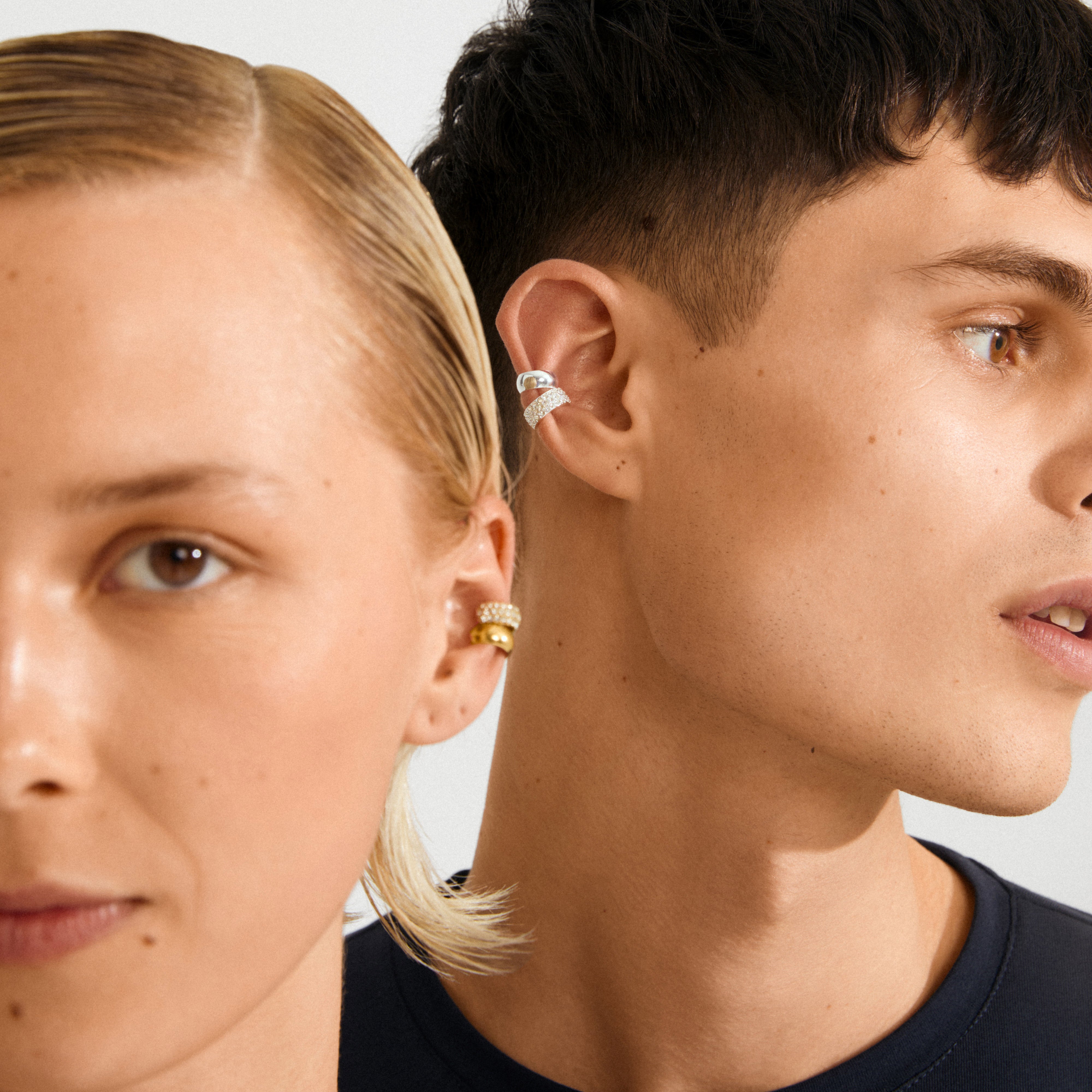 Two models showcasing HUDSYN ear cuff set: woman with gold cuffs, man with silver cuffs. Stylish, edgy jewelry for a trendy, piercing-free look.