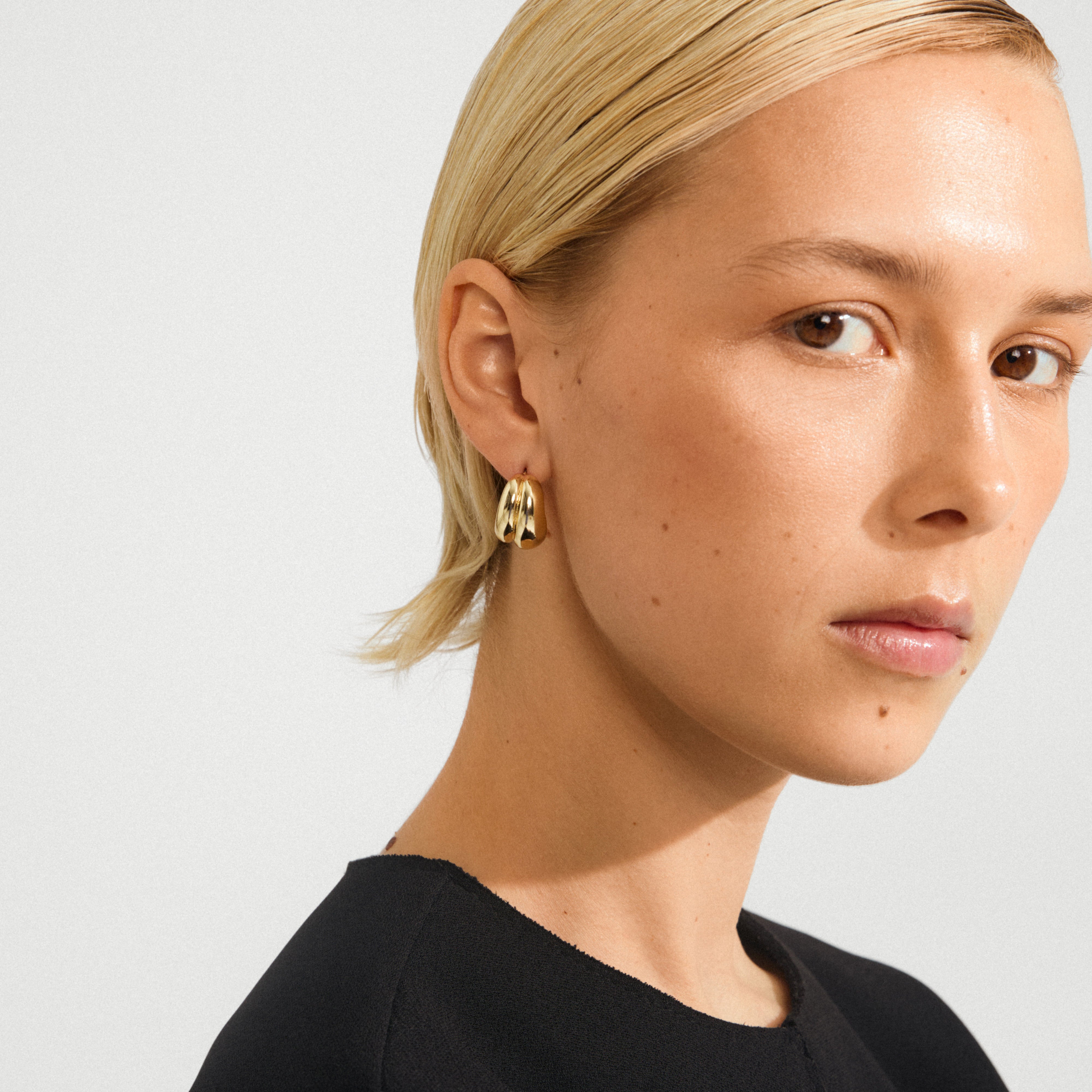 Person wearing MIKO gold-plated earrings—chunky, sleek hoops from Pilgrim, showcasing a sophisticated, modern style with an eco-conscious design for versatile elegance.